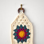 Crocheted wall hanging with a colorful flower design on a white background.