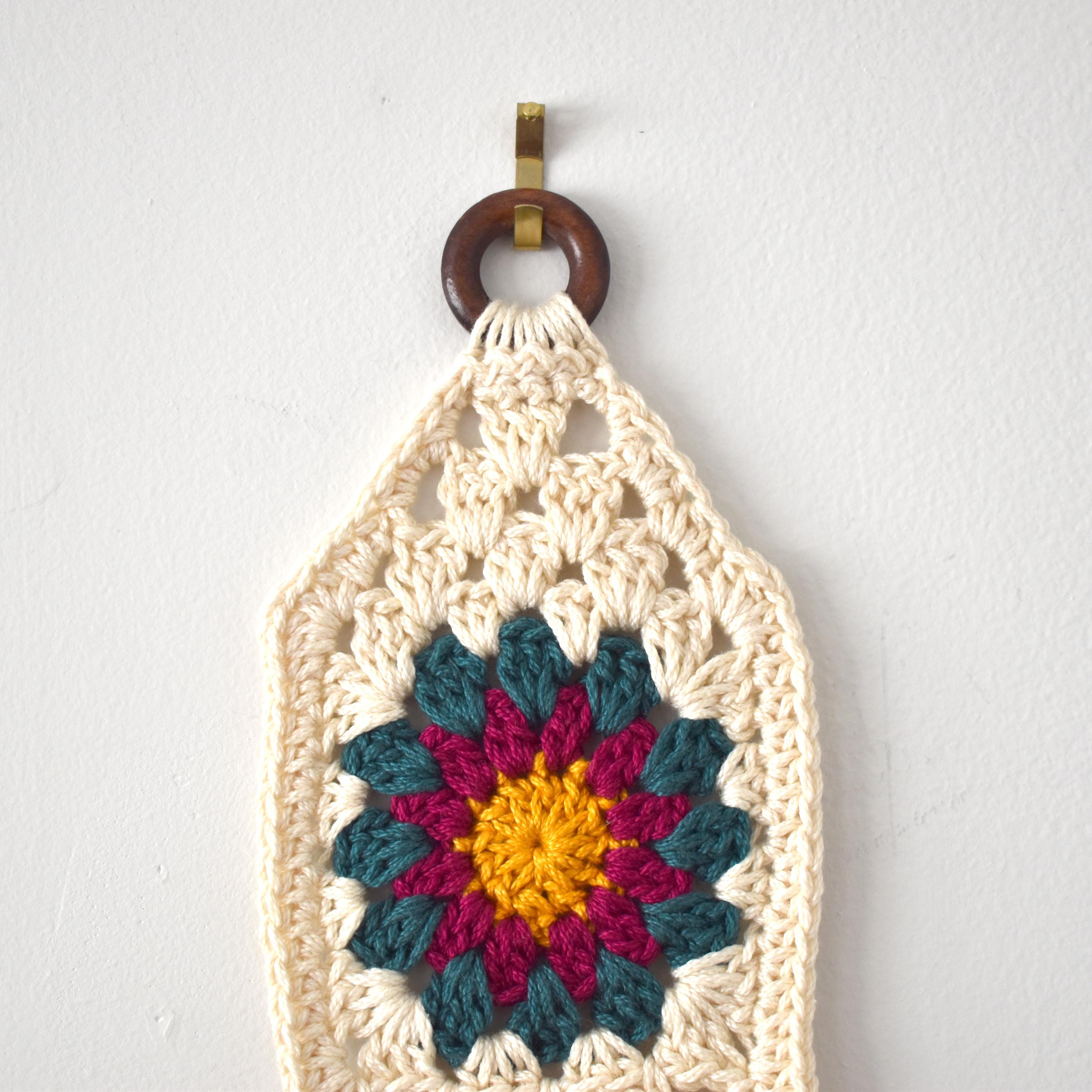 Crocheted wall hanging with a colorful flower design on a white background.