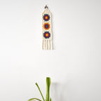Crocheted wall hanging with colorful floral patterns on a white background.