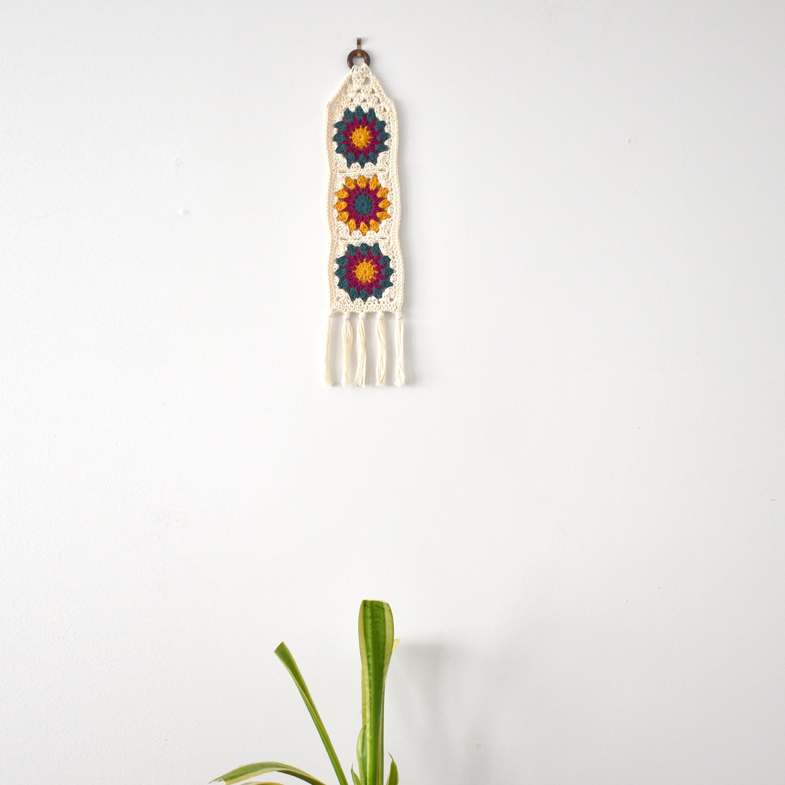 Crocheted wall hanging with colorful floral patterns on a white background.