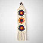 Crocheted wall hanging with colorful flower patterns on a white background.
