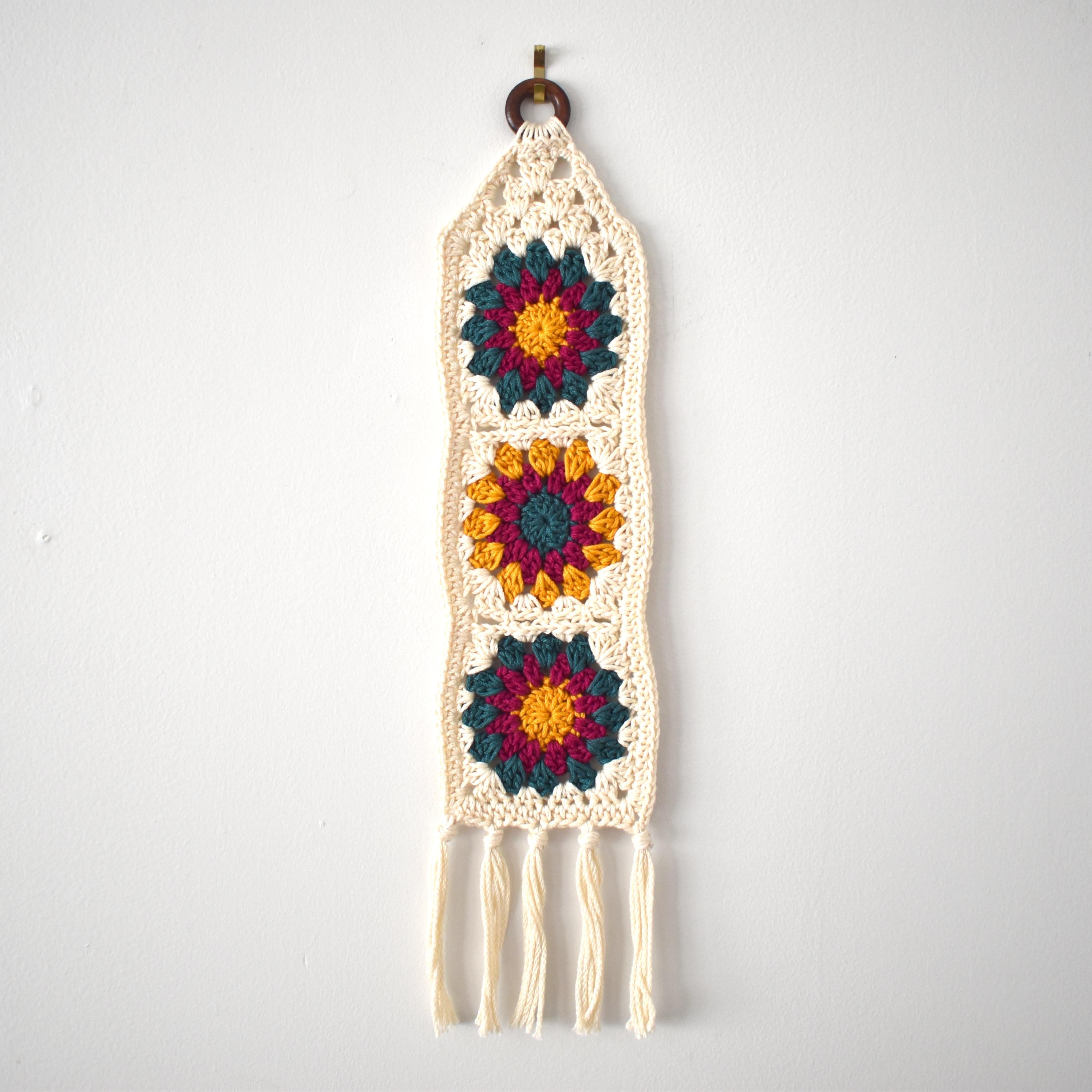 Crocheted wall hanging with colorful flower patterns on a white background.