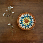 Crocheted coaster with a floral pattern on a wooden surface next to a branch of small white flowers.