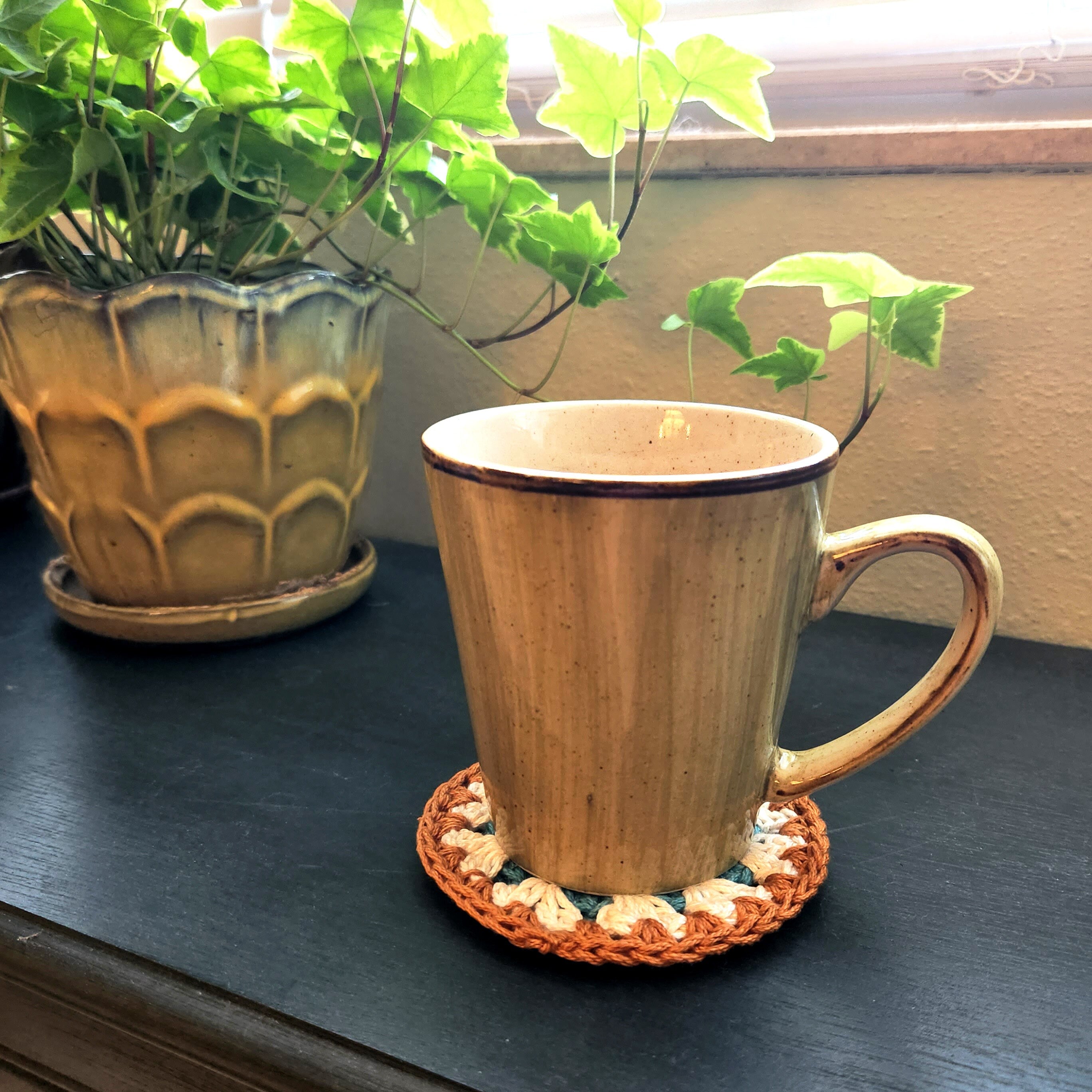 Ceramic mug on a crochet coaster with a plant in the background.