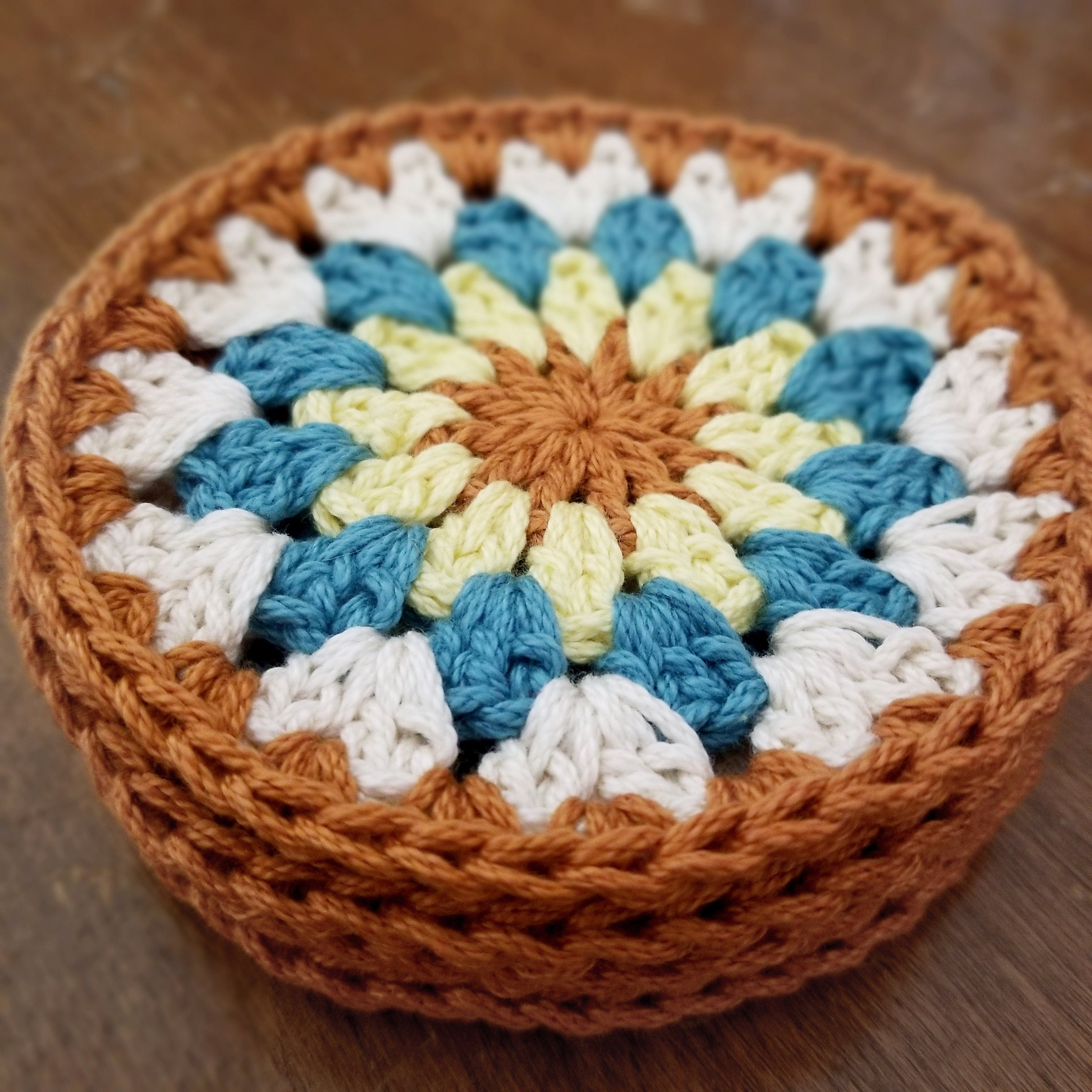 Stack of crocheted coasters with a colorful sunflower pattern on a wooden surface.
