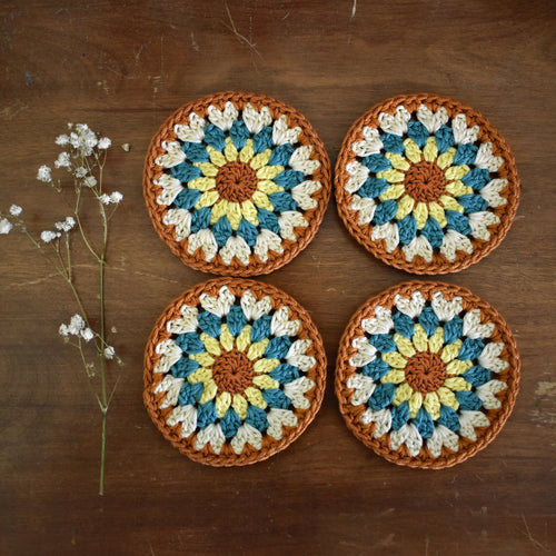 Four crocheted coasters with a floral pattern on a wooden surface.