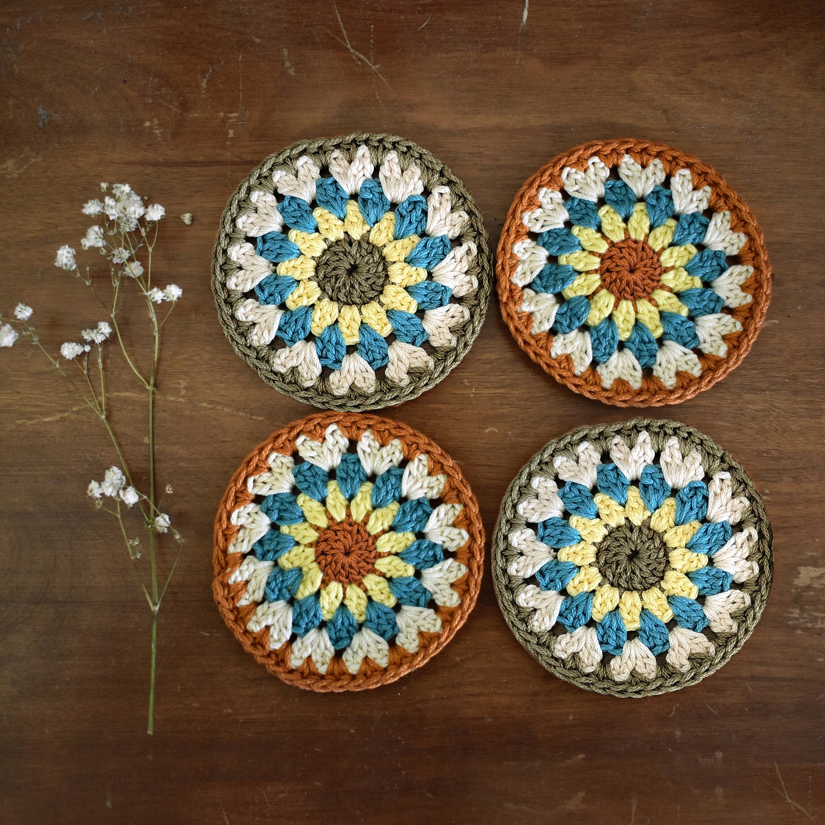 Four crocheted coasters with a floral pattern on a wooden surface.