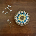 Crocheted coaster with floral pattern on a wooden surface next to a branch of small white flowers.