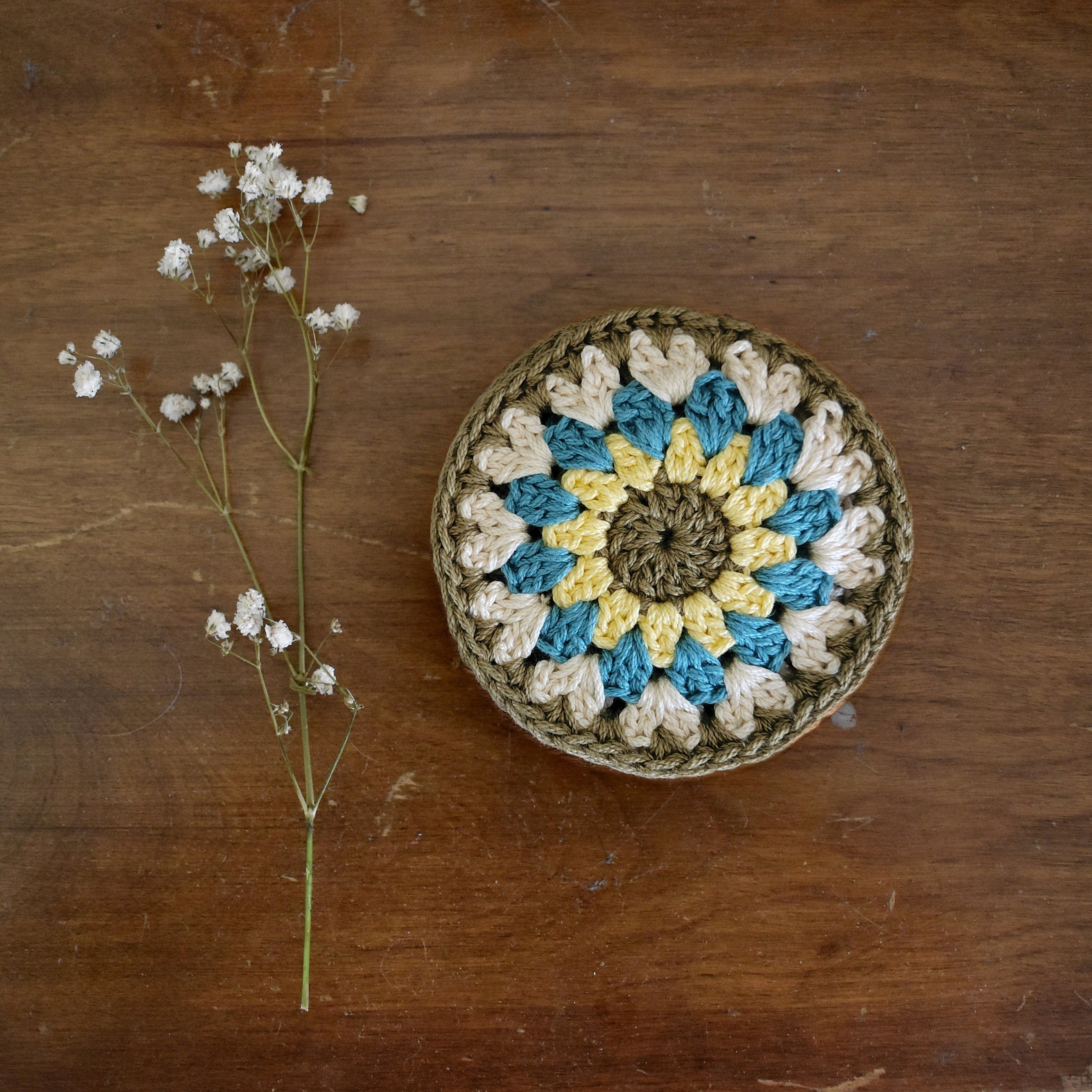 Crocheted coaster with floral pattern on a wooden surface next to a branch of small white flowers.