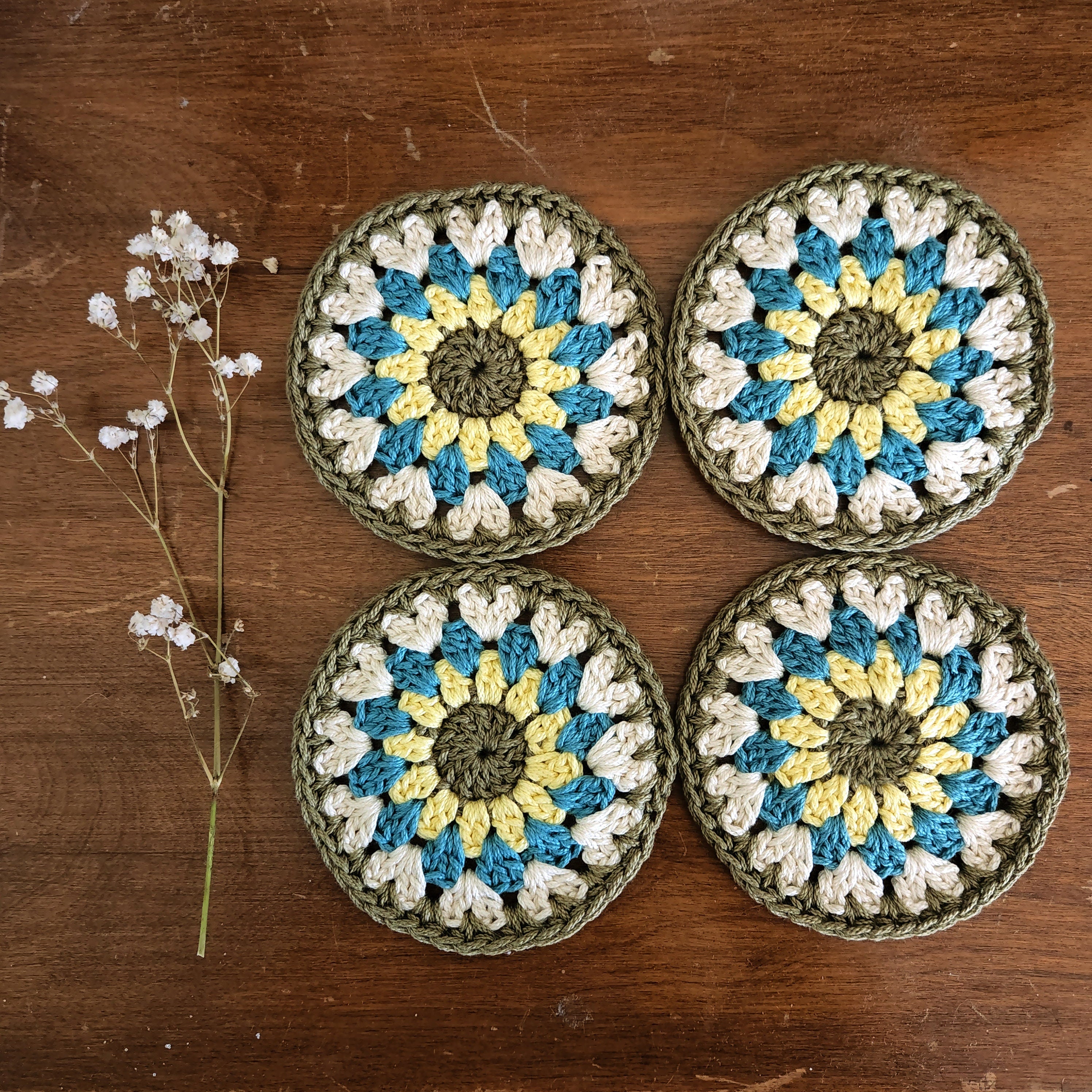 Four crocheted coasters with a floral pattern on a wooden surface.