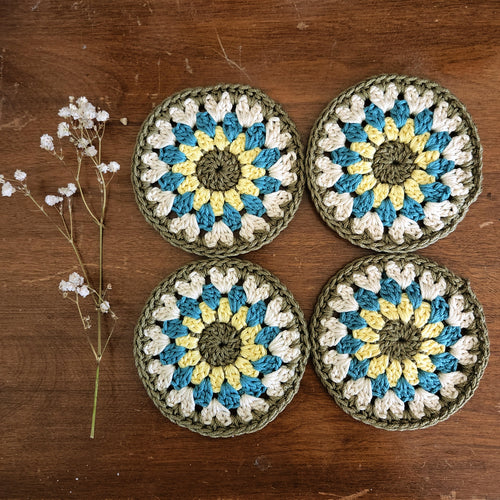 Four crocheted coasters with a floral pattern on a wooden surface.