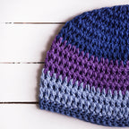 Close-up view of a crocheted beanie with a blue and purple gradient on a white wooden surface.