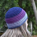 Person wearing a blue and purple striped knit beanie with a blurred green outdoor background.