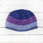 Crocheted beanie with a blue-and-purple gradient on a white wooden surface.