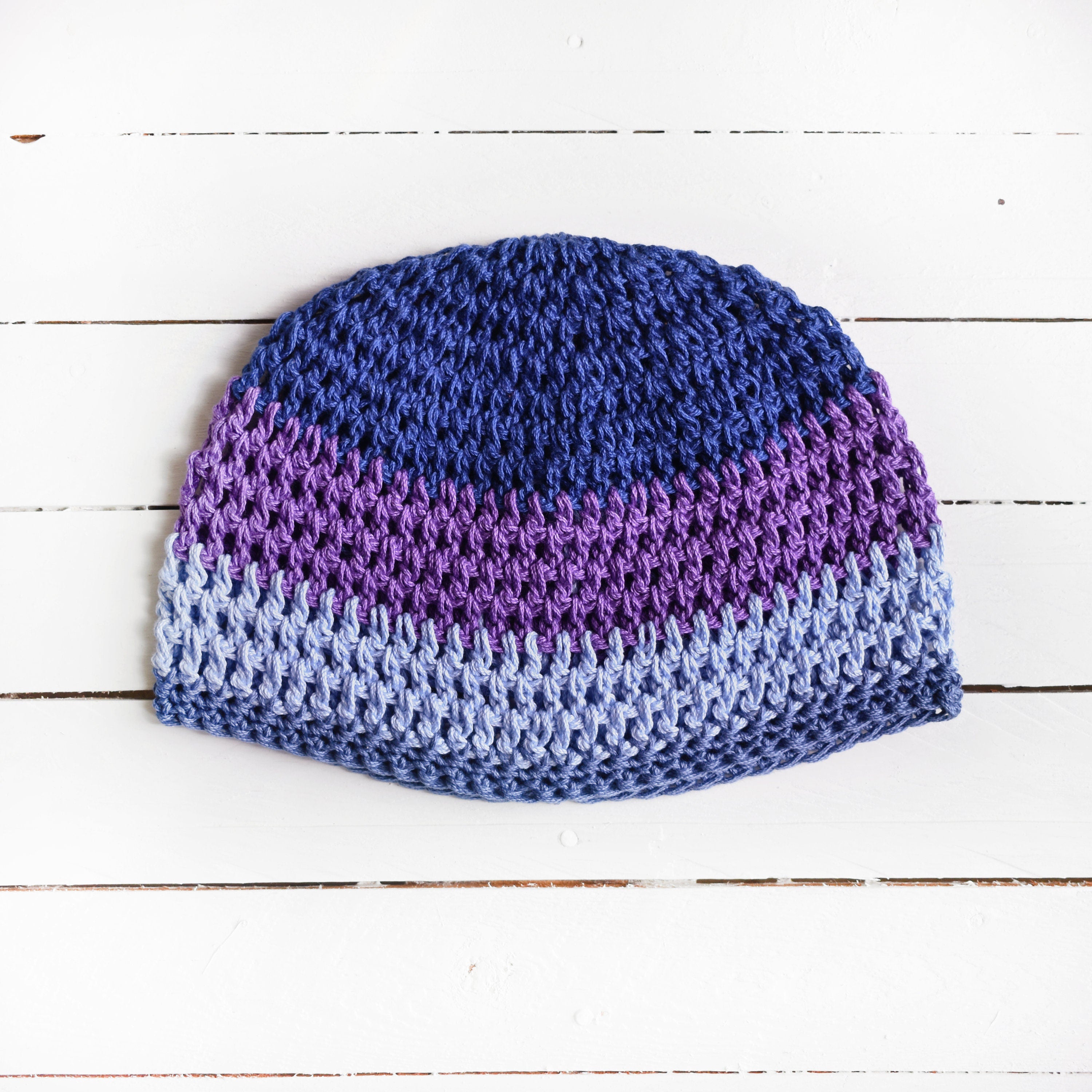 Crocheted beanie with a blue-and-purple gradient on a white wooden surface.