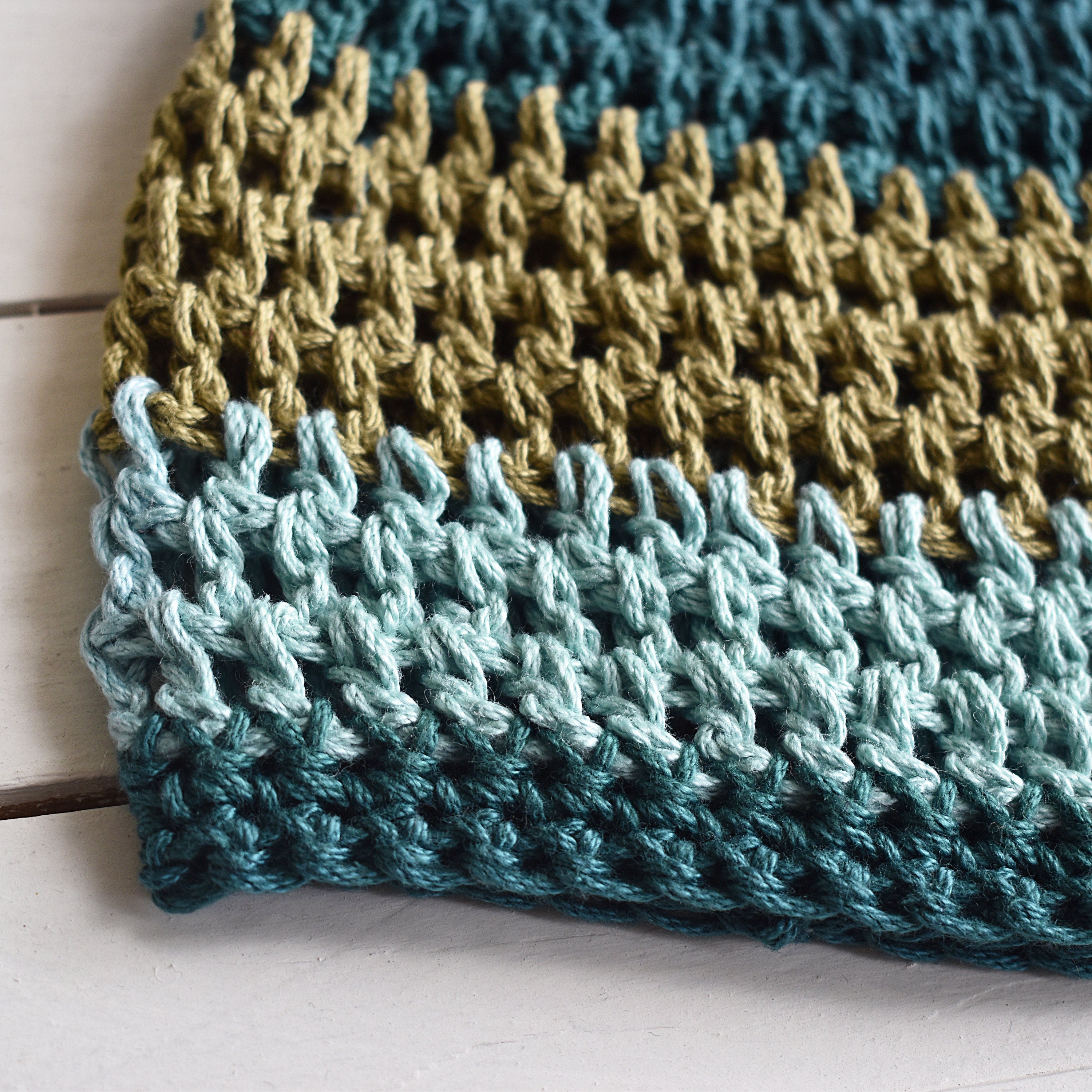 Close-up of a crocheted hat with teal and green stripes on a wooden surface.