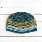 Crocheted beanie with teal and green striped colors on a wooden surface.