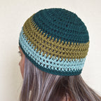 A woman wearing a teal and green striped beanie against a neutral background.