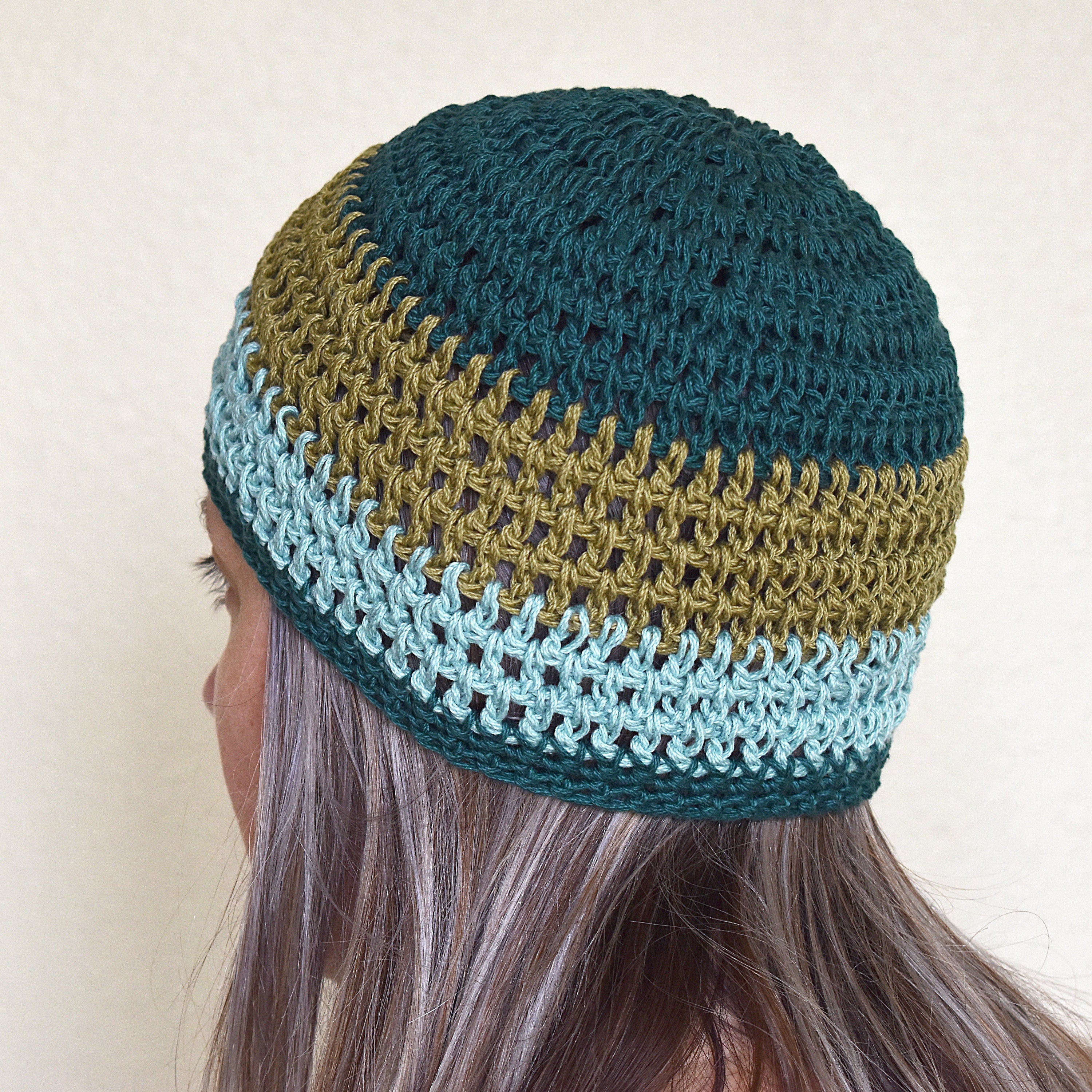 A woman wearing a teal and green striped beanie against a neutral background.