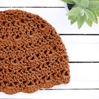 Orange crocheted hat on a white wooden surface with a green plant in the corner.
