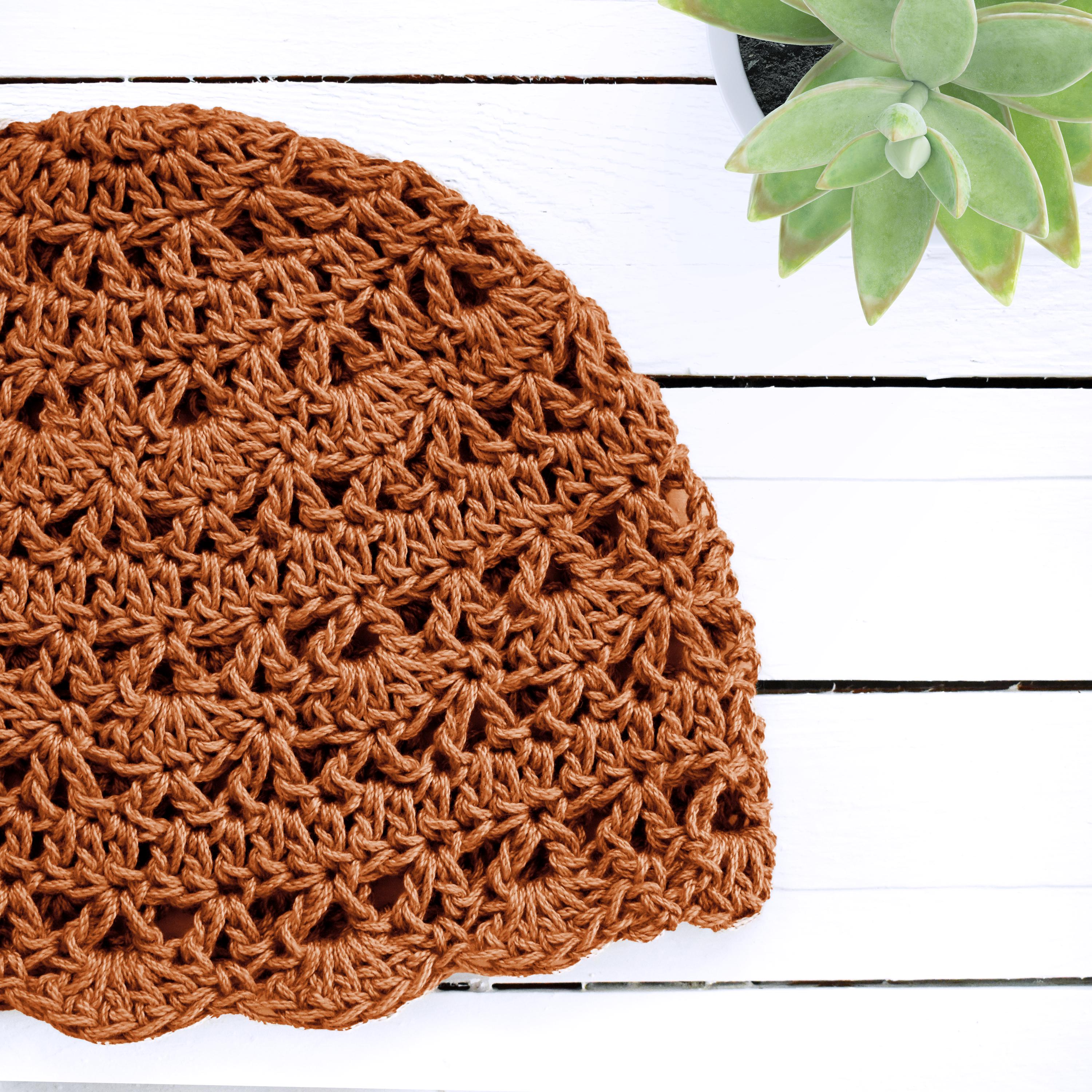 Orange crocheted hat on a white wooden surface with a green plant in the corner.