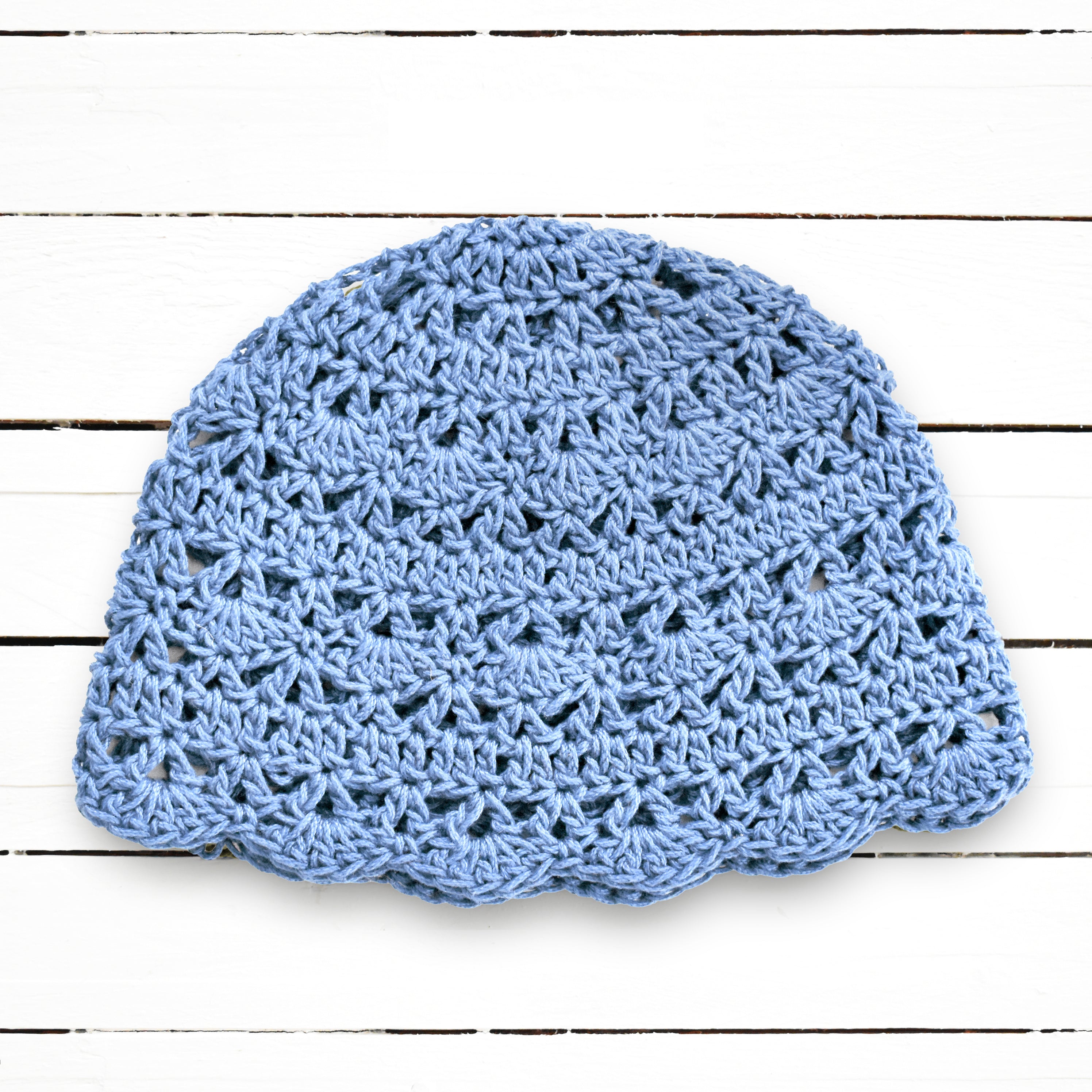 Baby blue crocheted hat on a white wooden surface.