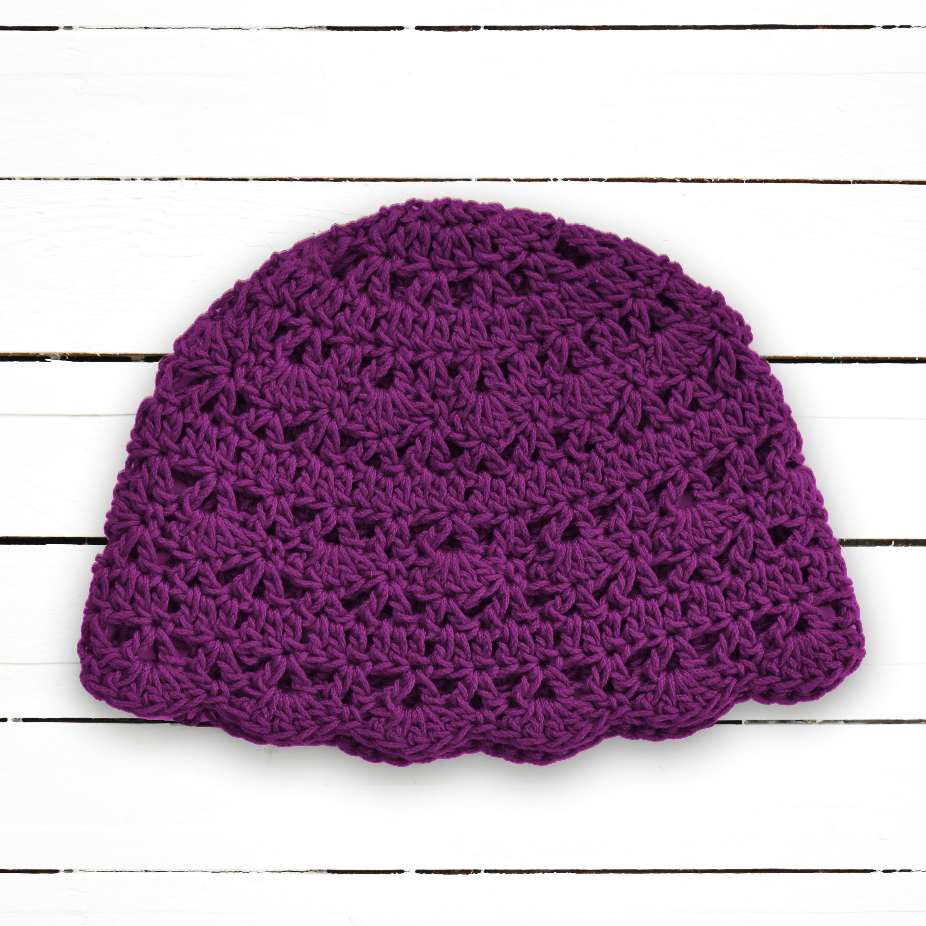 Dark purple crocheted beanie on a white wooden background.