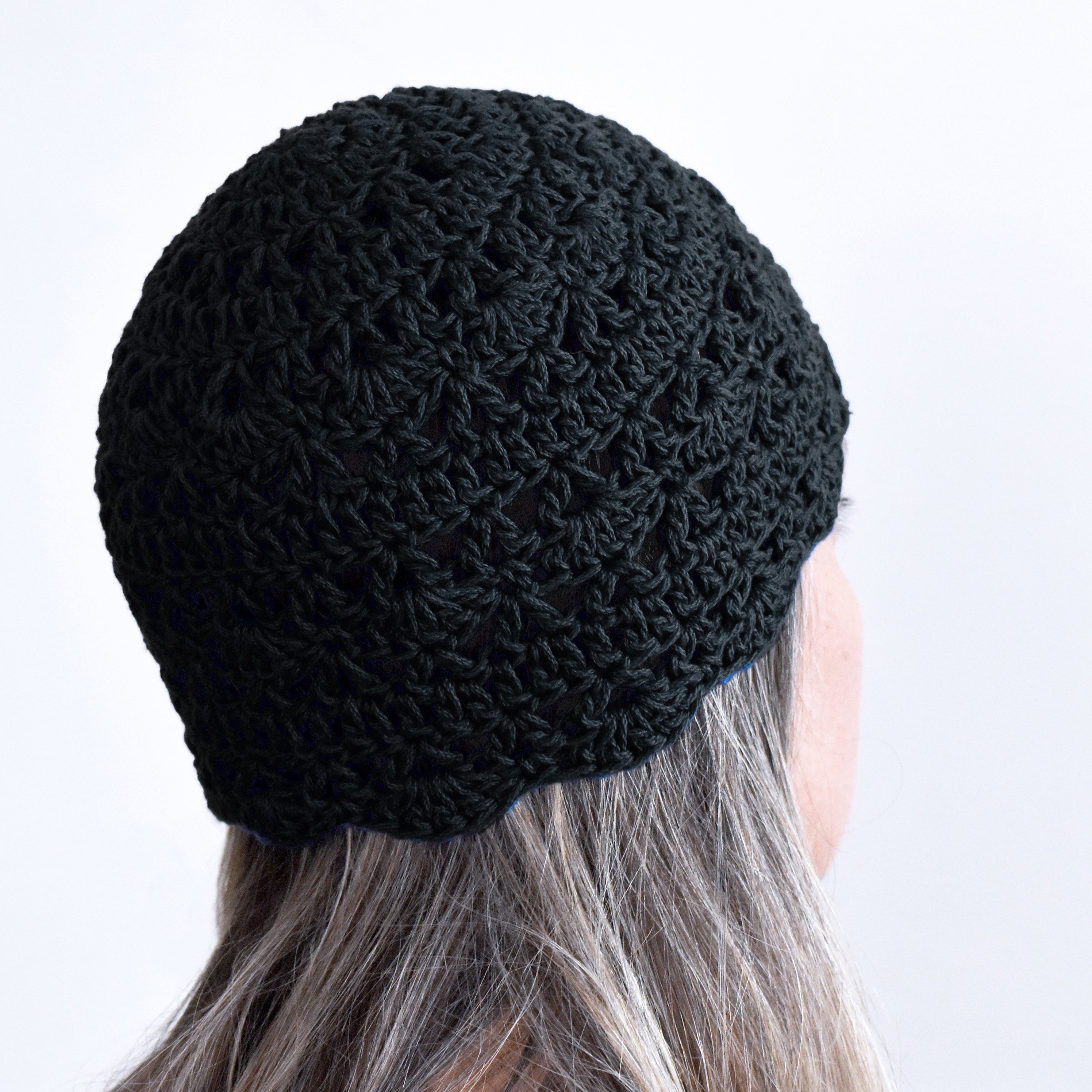 Black knitted beanie worn by a person with light hair on a white background.