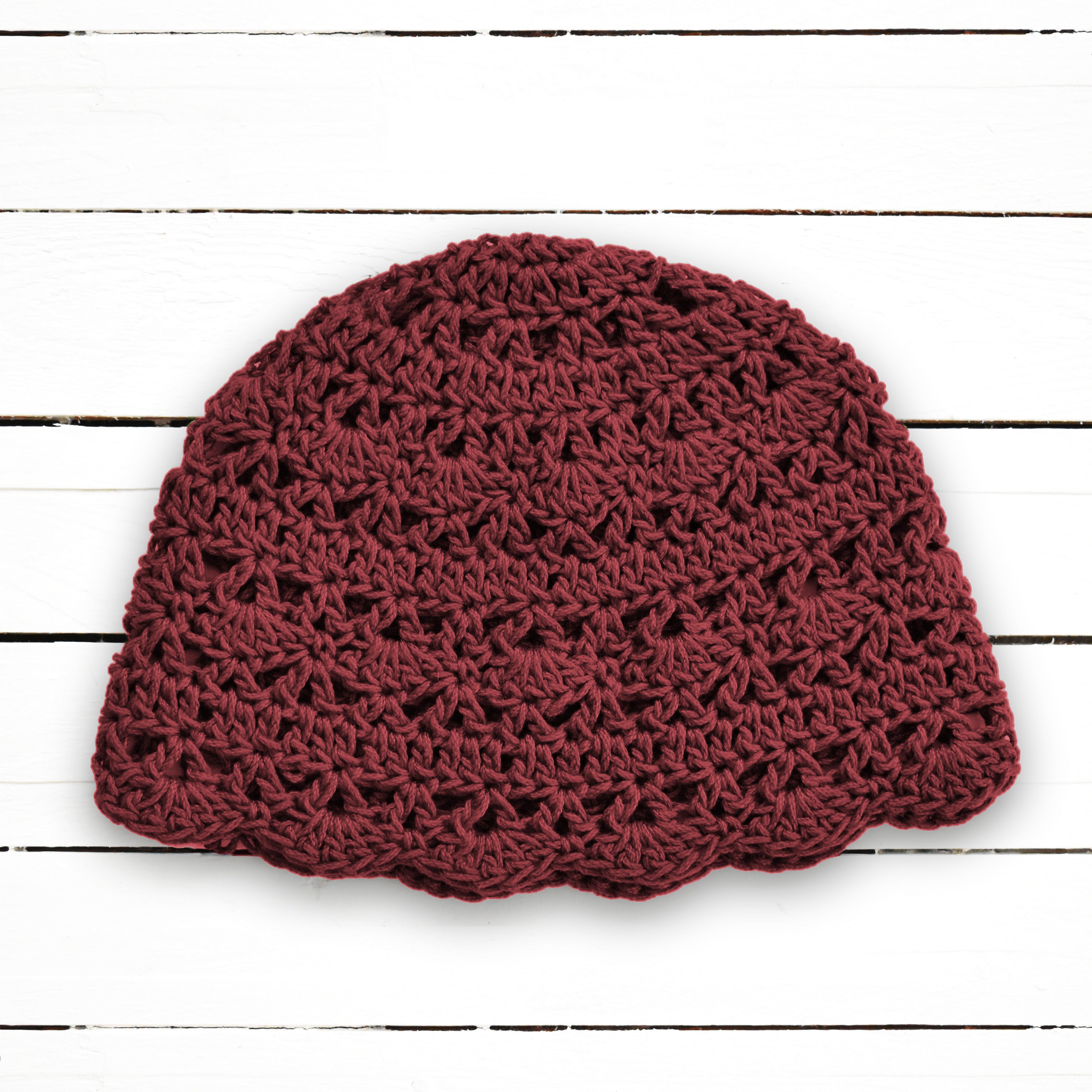 Burgundy red crochet lace beanie on a white wooden background.