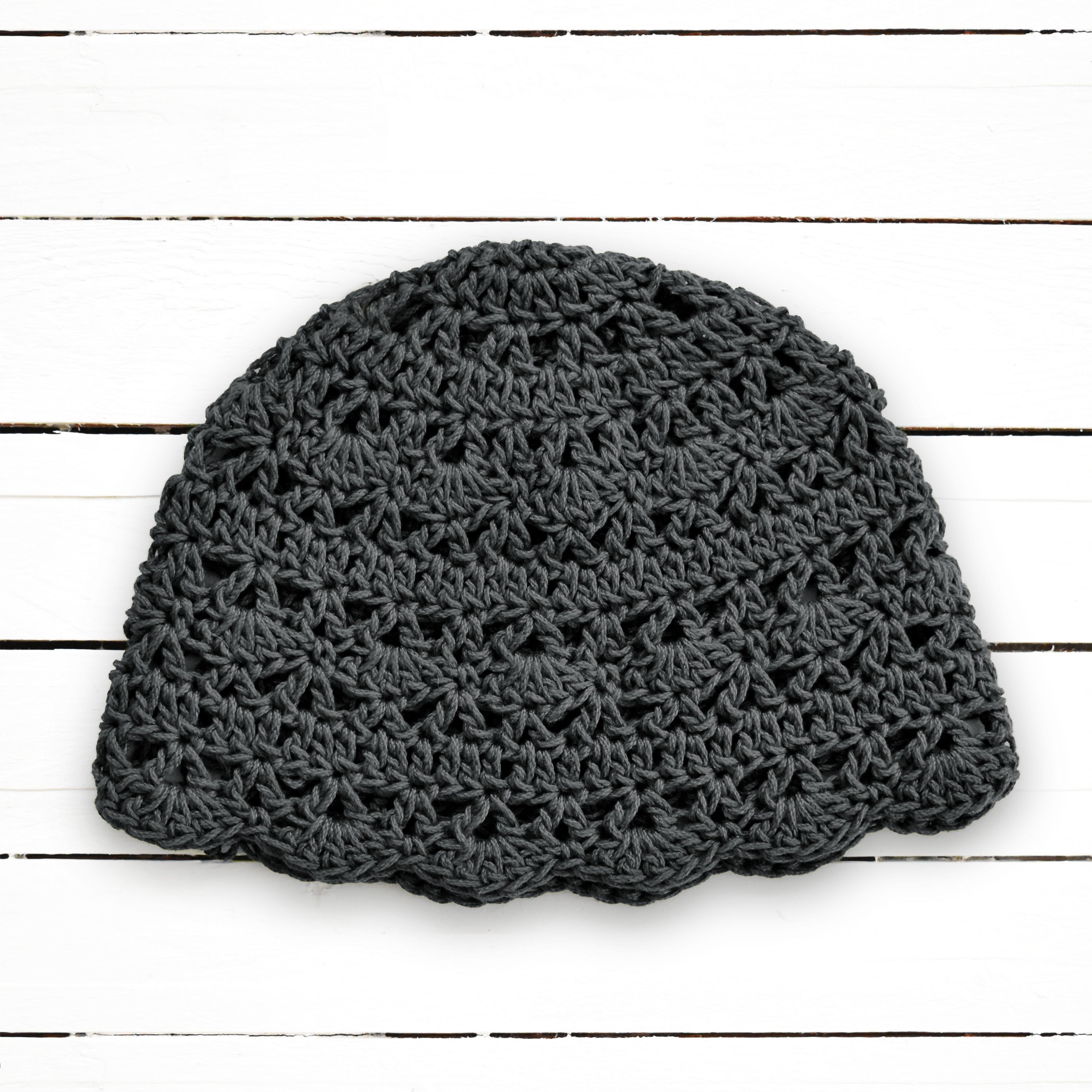 Dark gray crochet beanie on a white wooden surface.