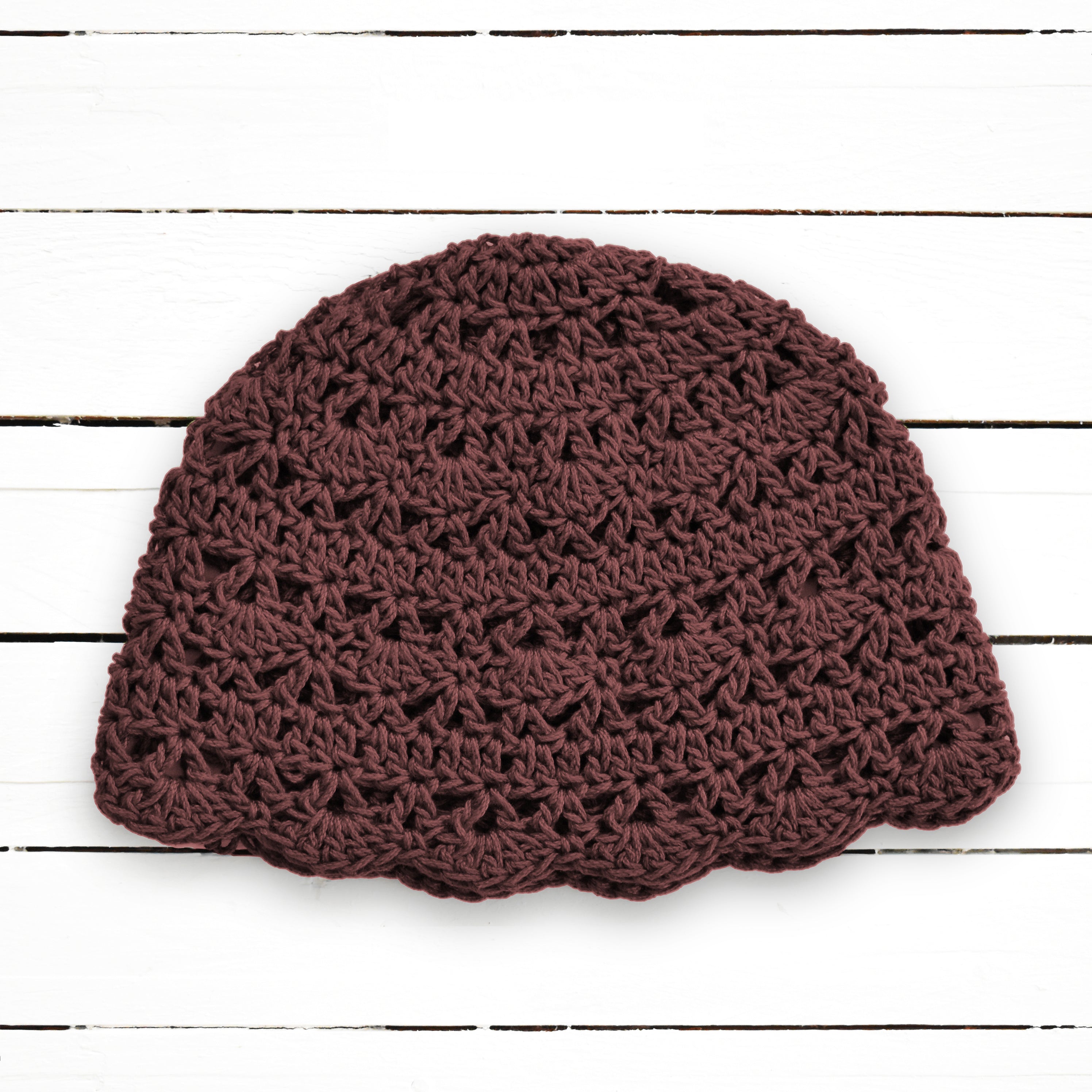 Brown crocheted beanie on a white wooden background.