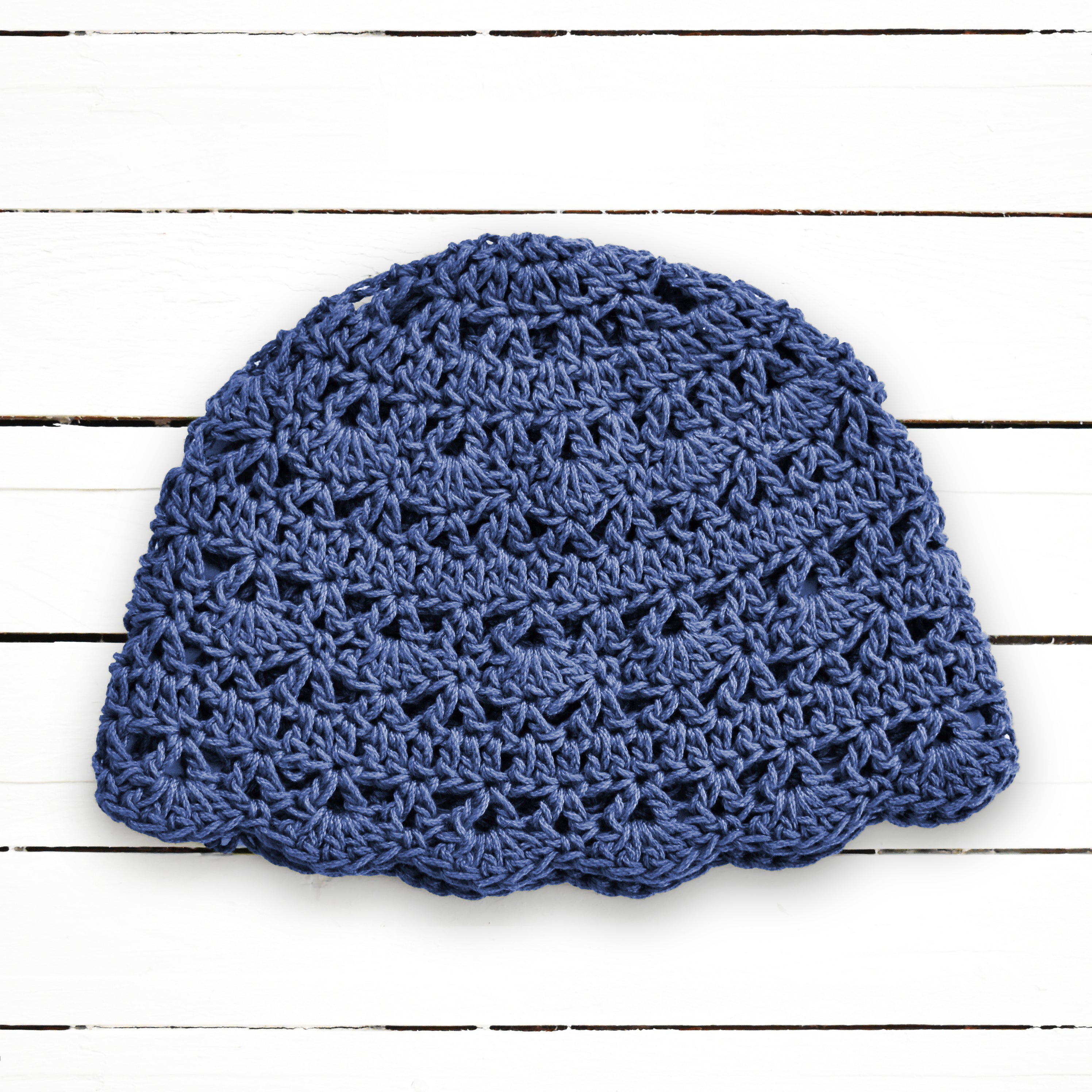 Denim blue crochet beanie on a white wooden background.
