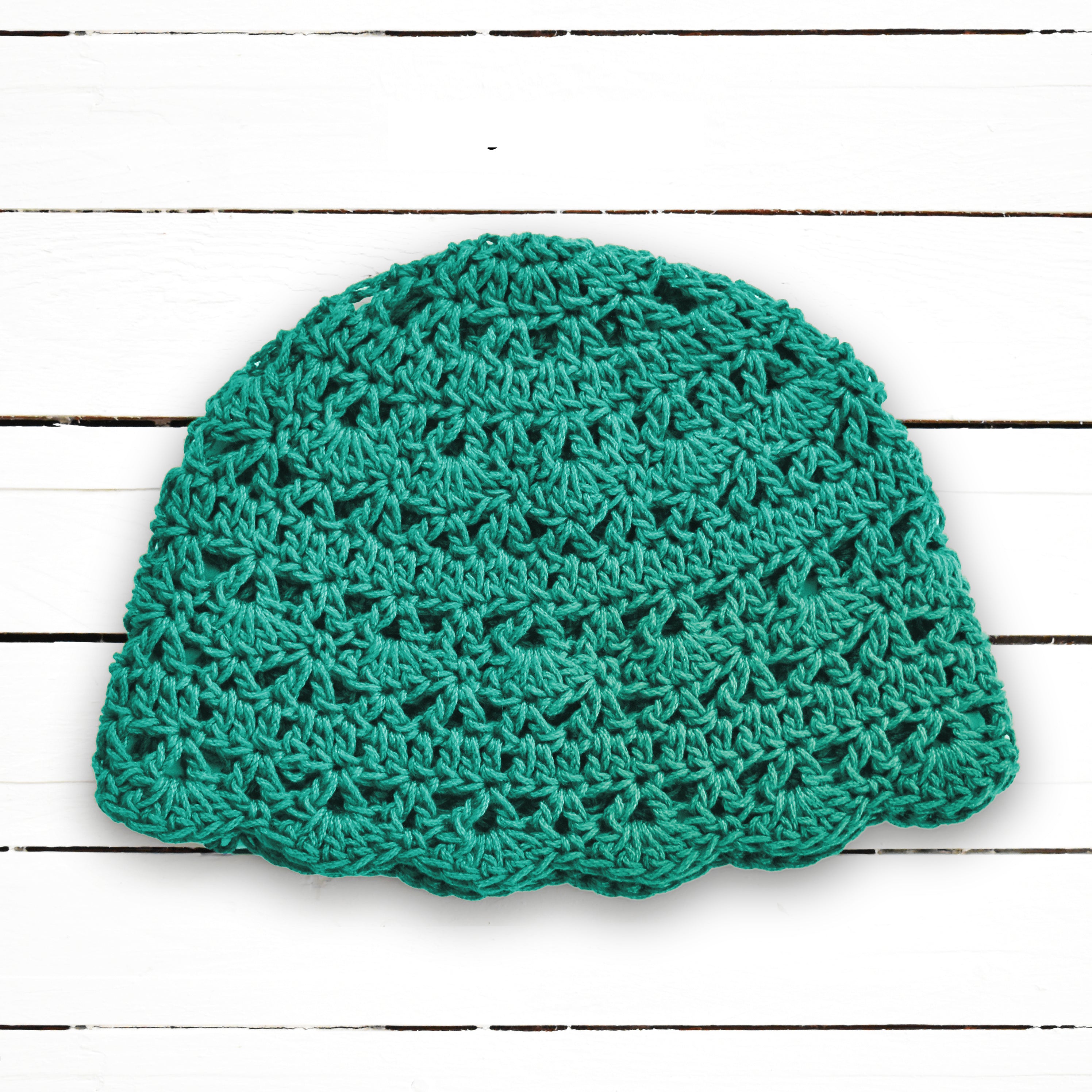 Light teal crochet beanie on a white wooden background.