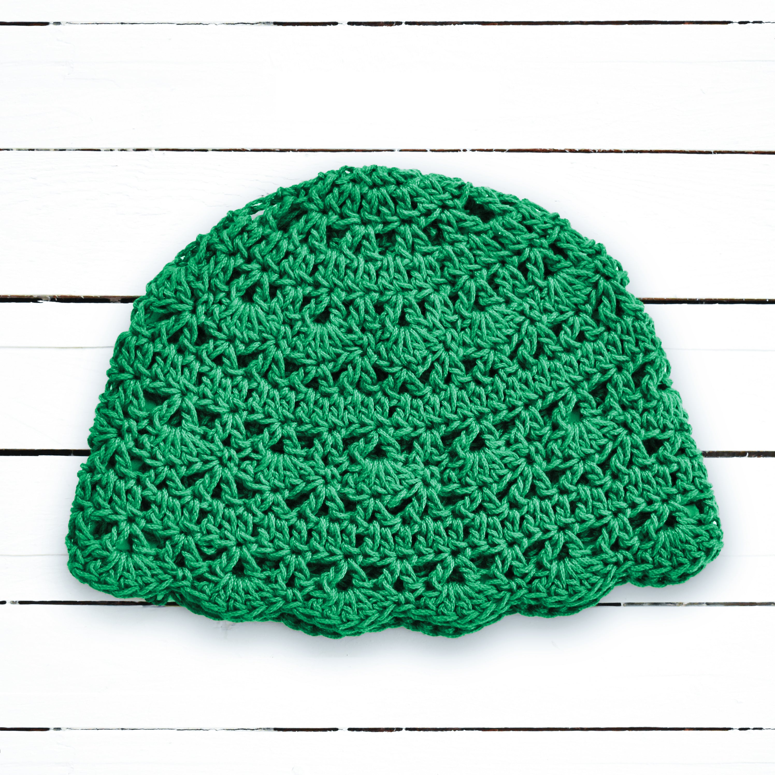 Green lace crocheted beanie on a white wooden background.