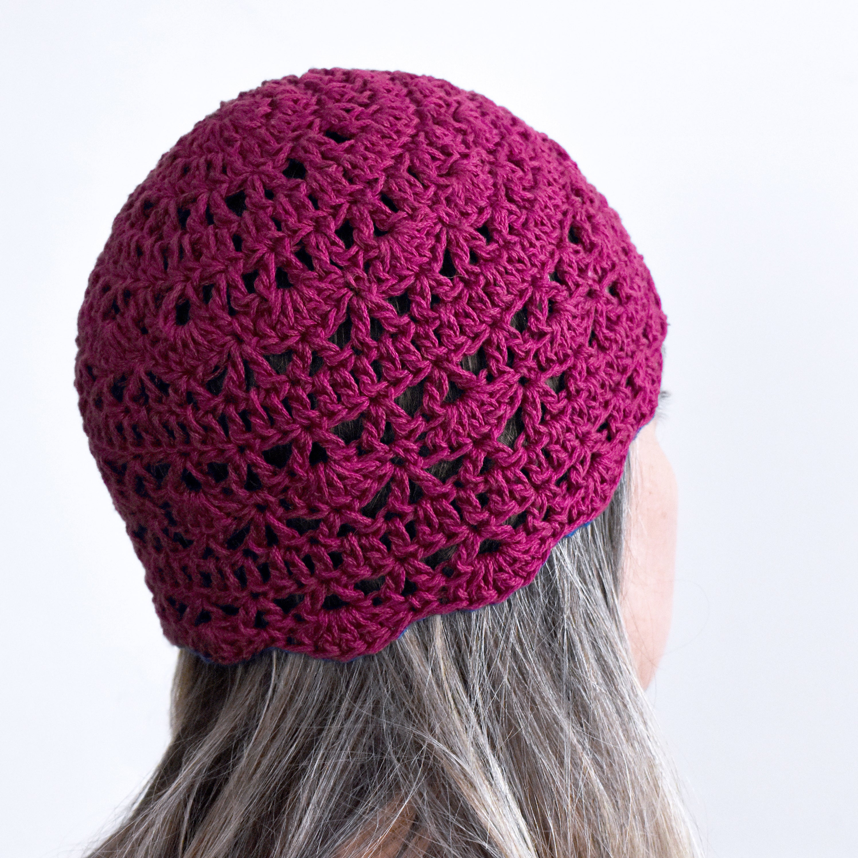 Close-up of a magenta pink knitted beanie on a person with a white background.