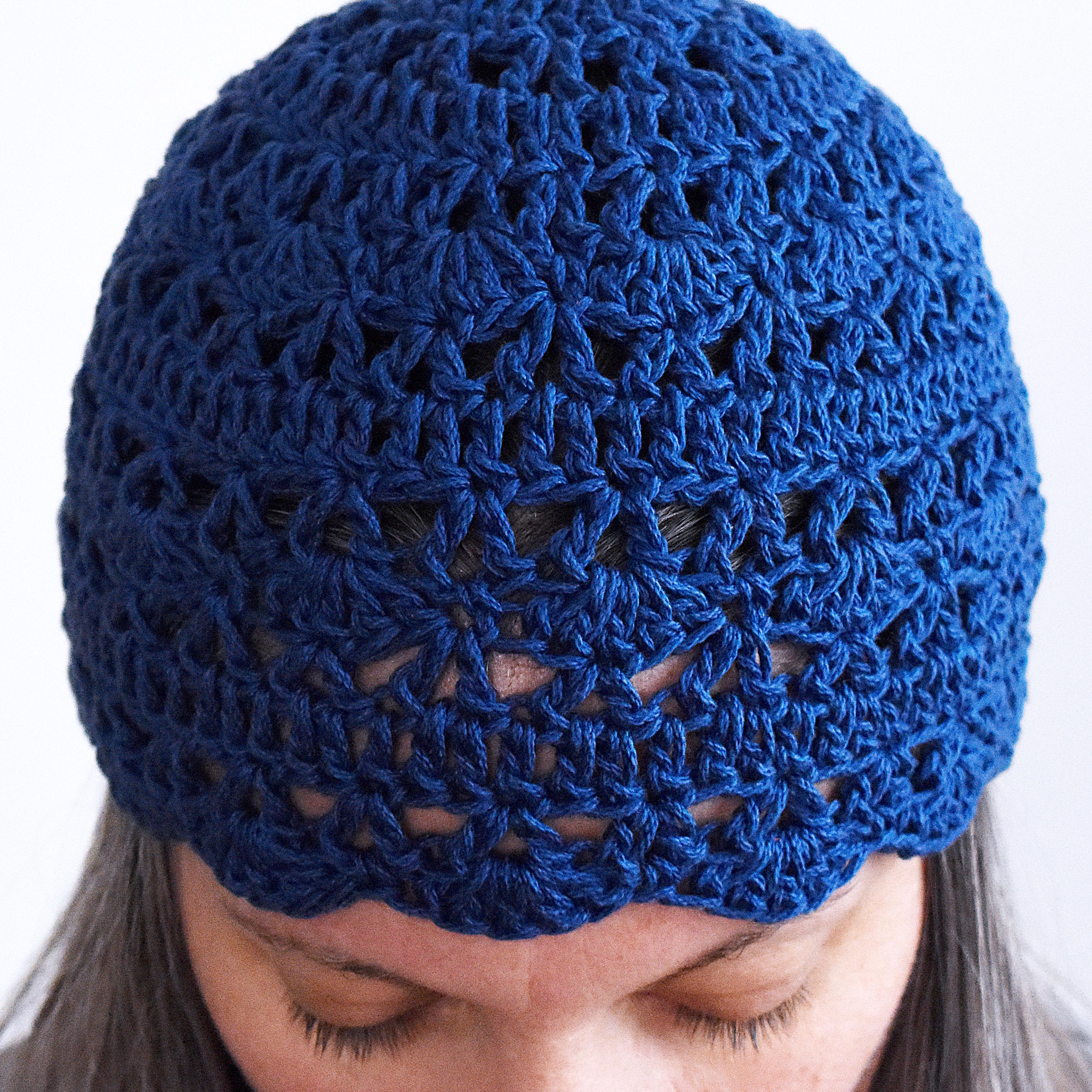 Close-up of a blue knitted beanie worn by a woman against a white background.