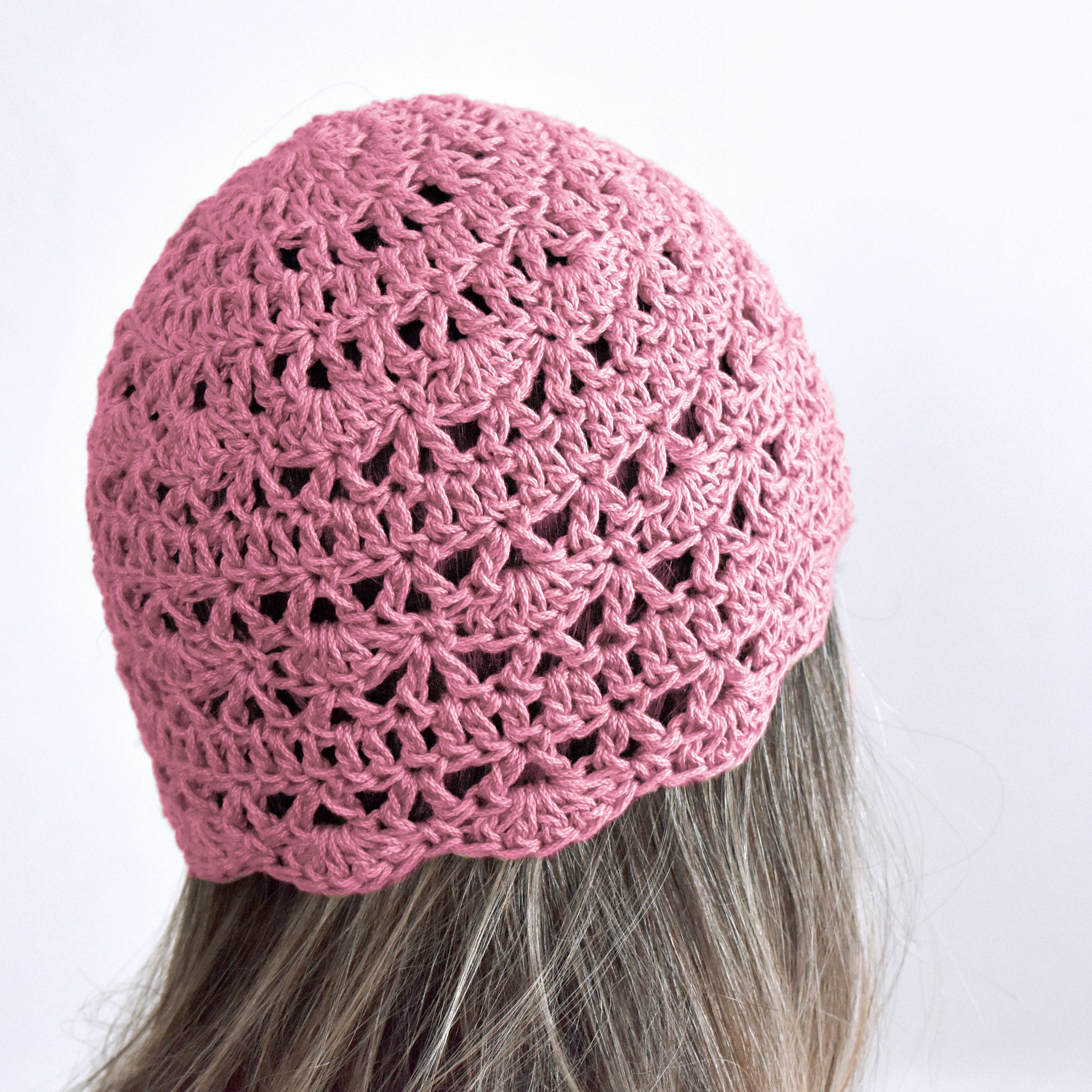 Pink crocheted beanie worn by a person with gray hair on a white background.