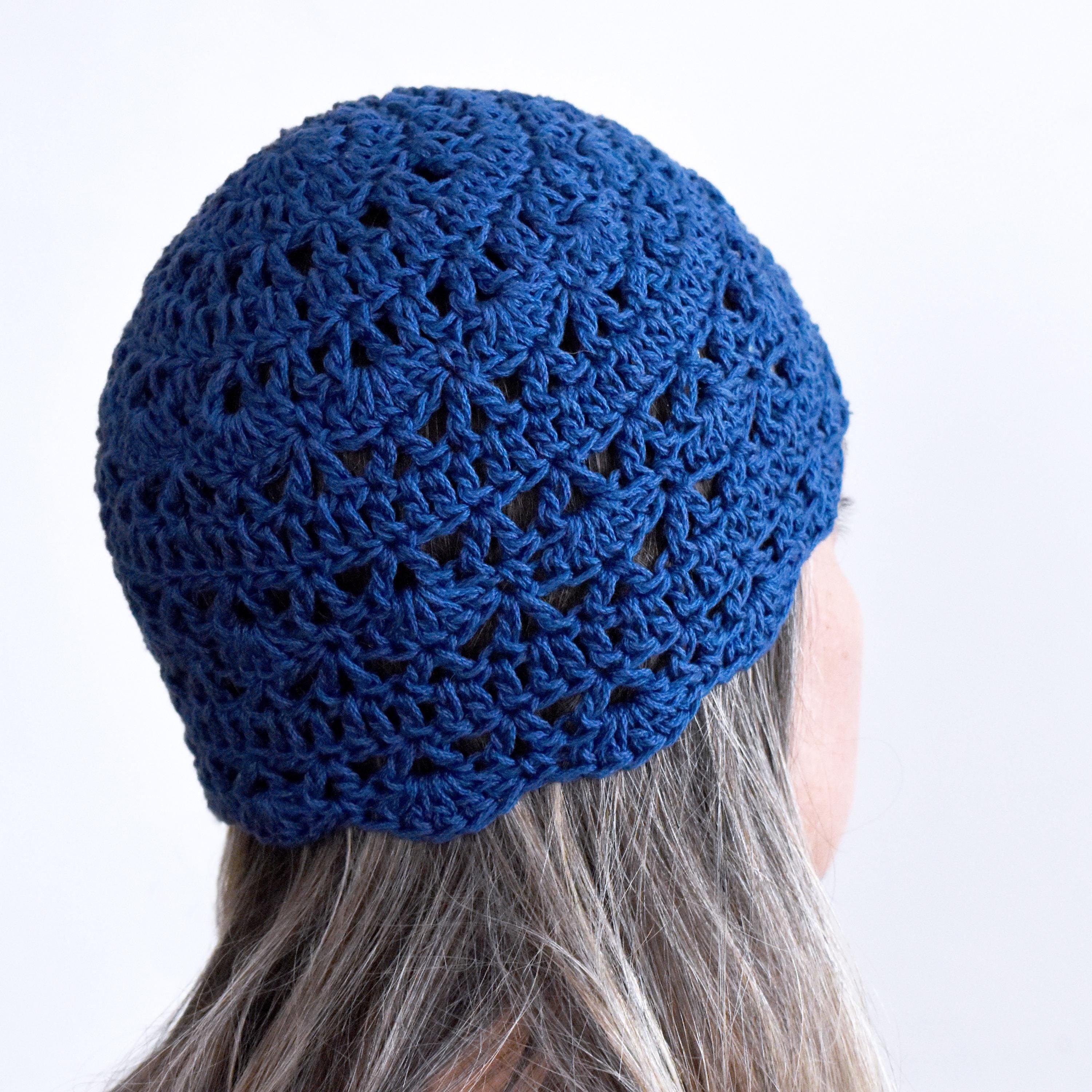 Blue crocheted beanie worn by a person with light gray hair against a white background.