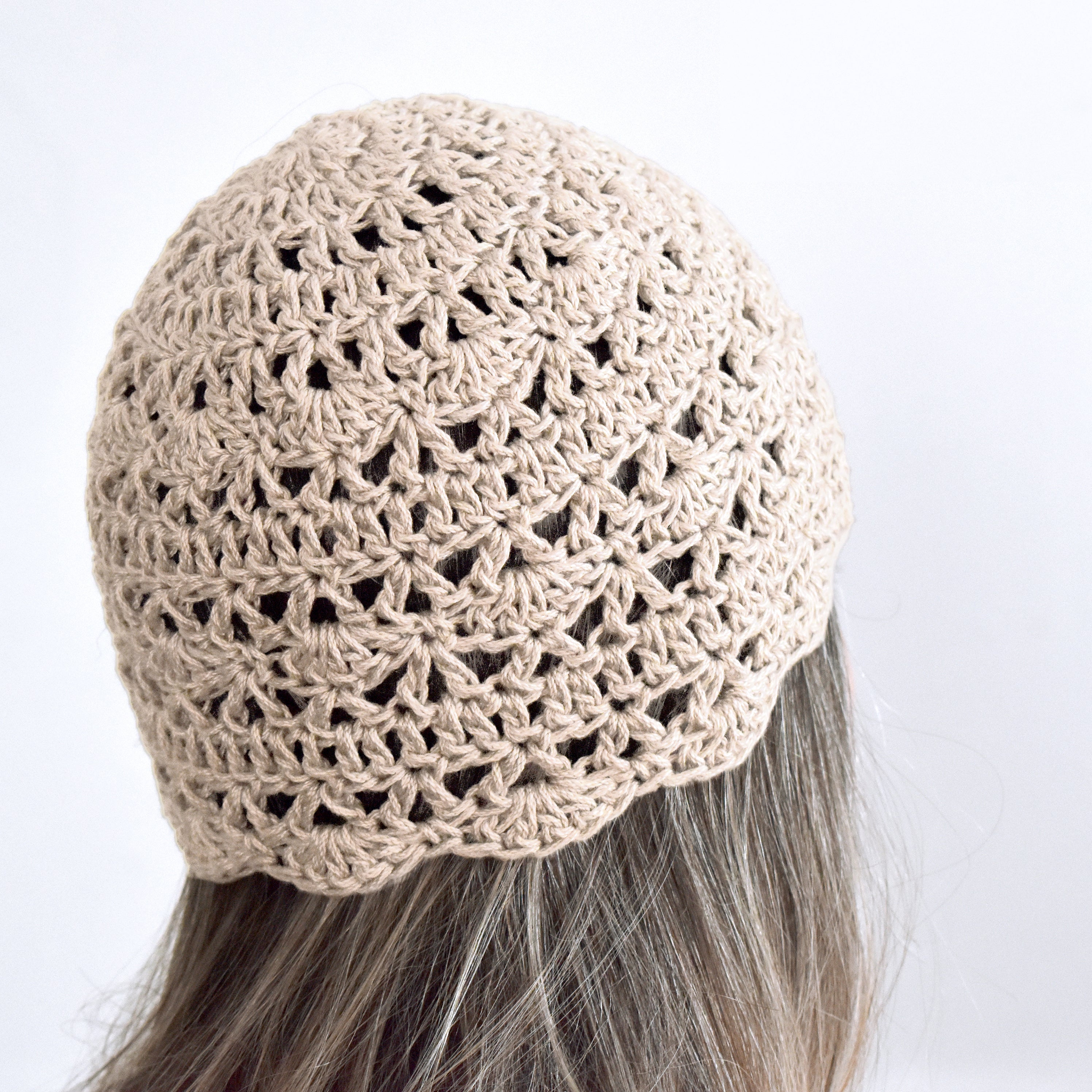 Beige crochet hat worn by a person with gray hair on a white background.