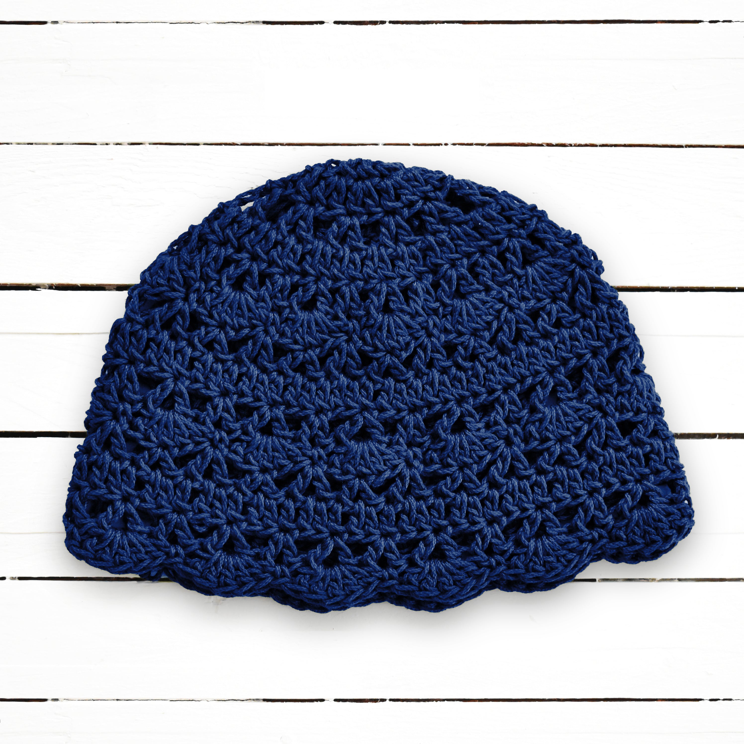 Navy blue crocheted beanie on a white wooden background.