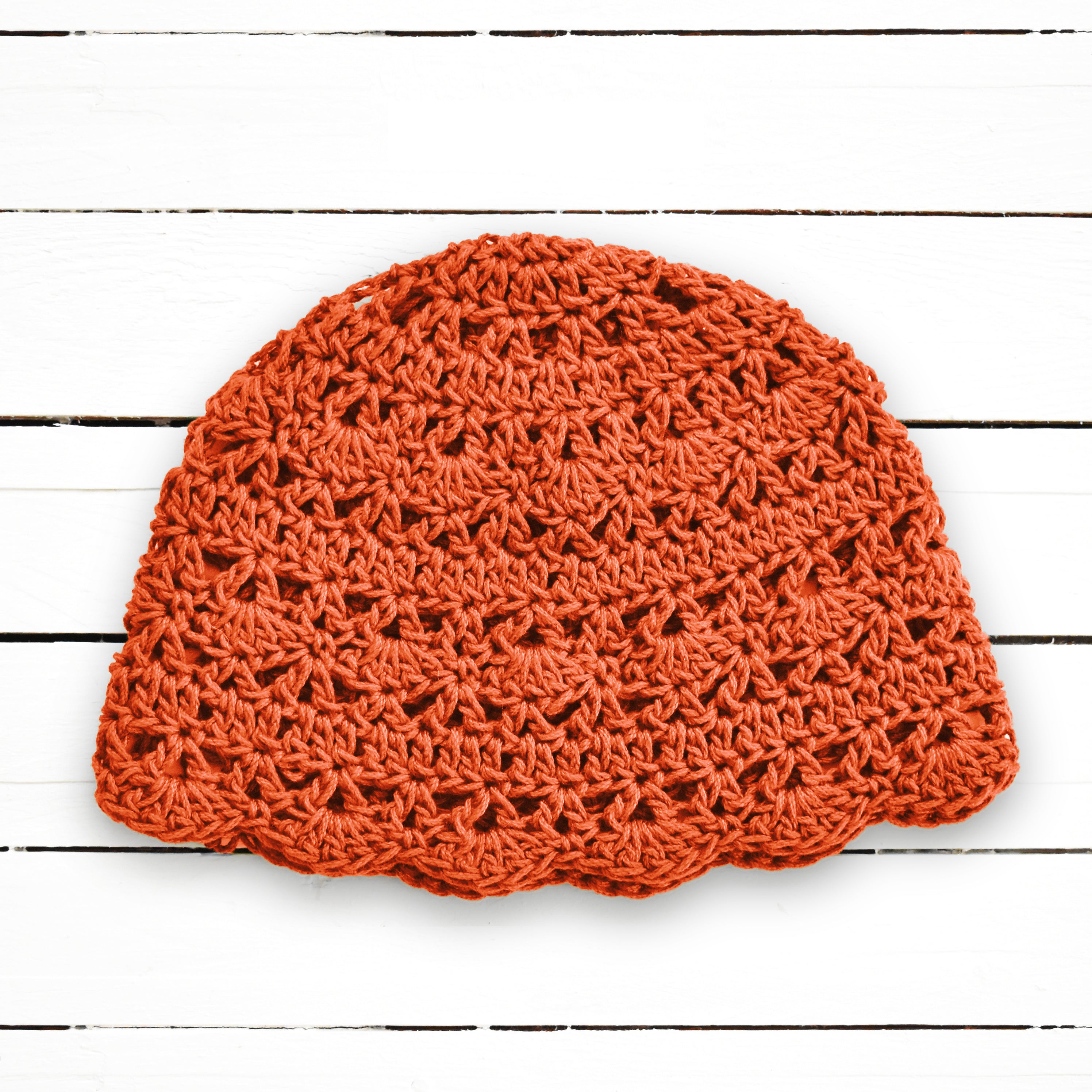 Orange crochet beanie on a white wooden surface.