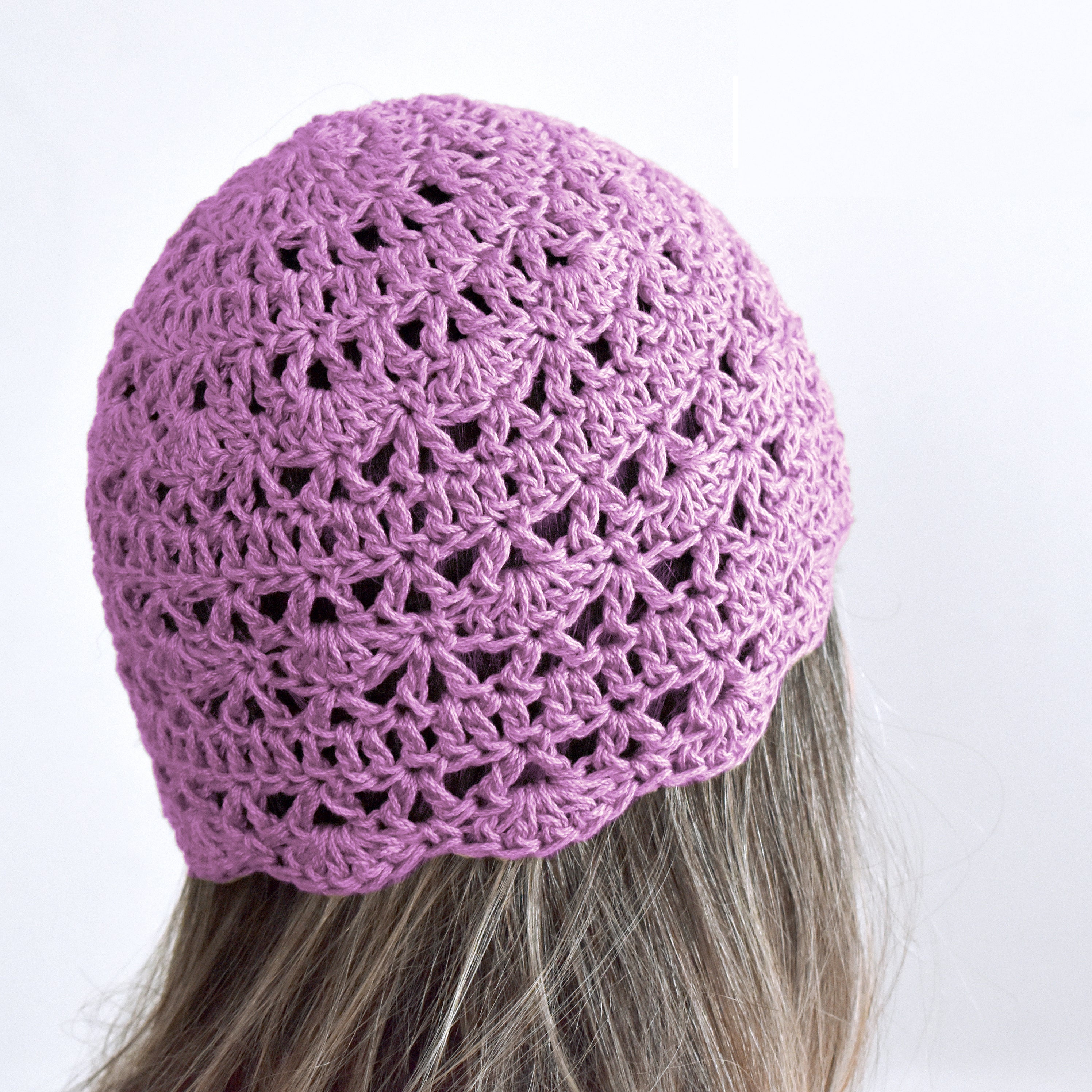 Light purple crocheted beanie worn by a person with gray hair on a white background.