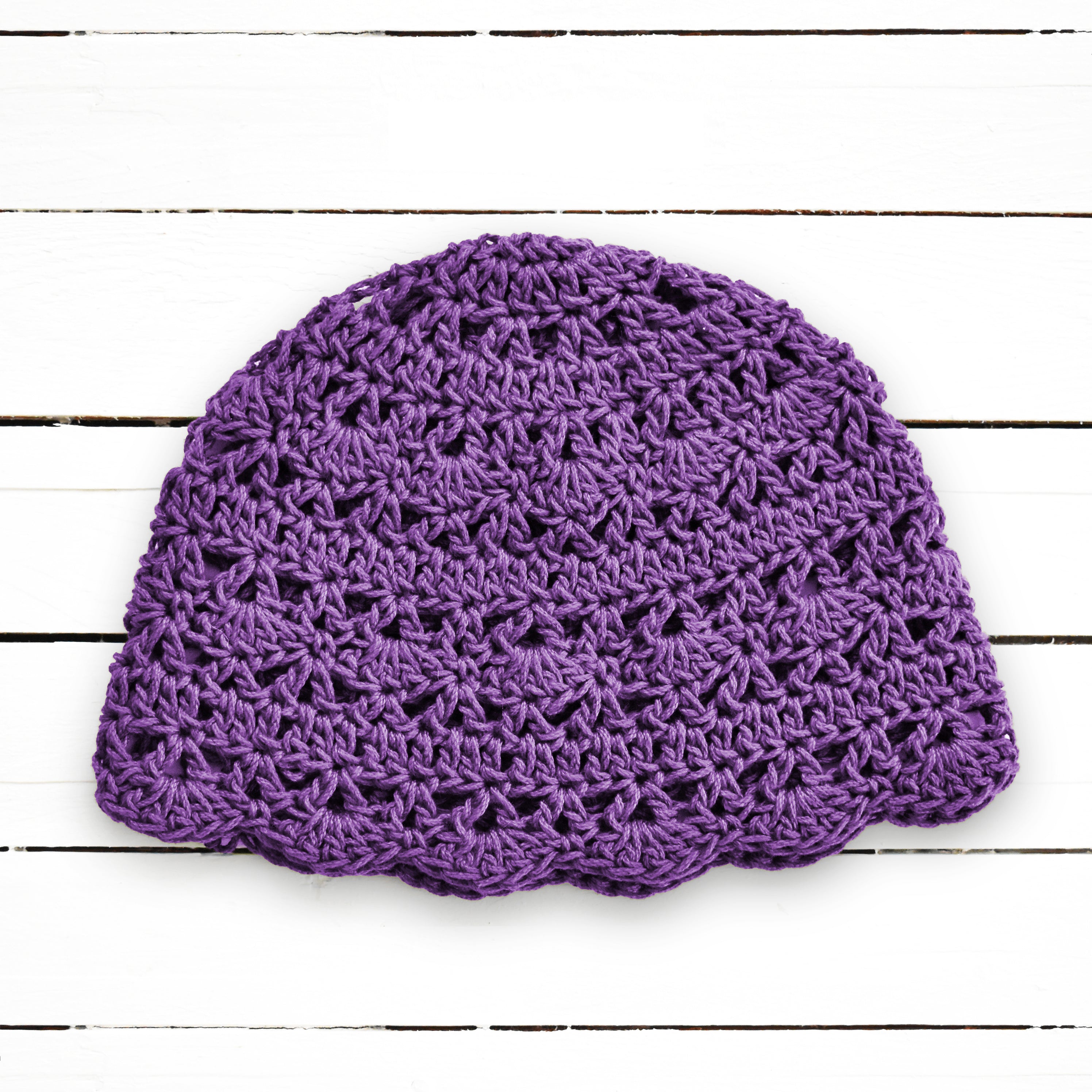 Purple crocheted lace beanie on a wooden surface.