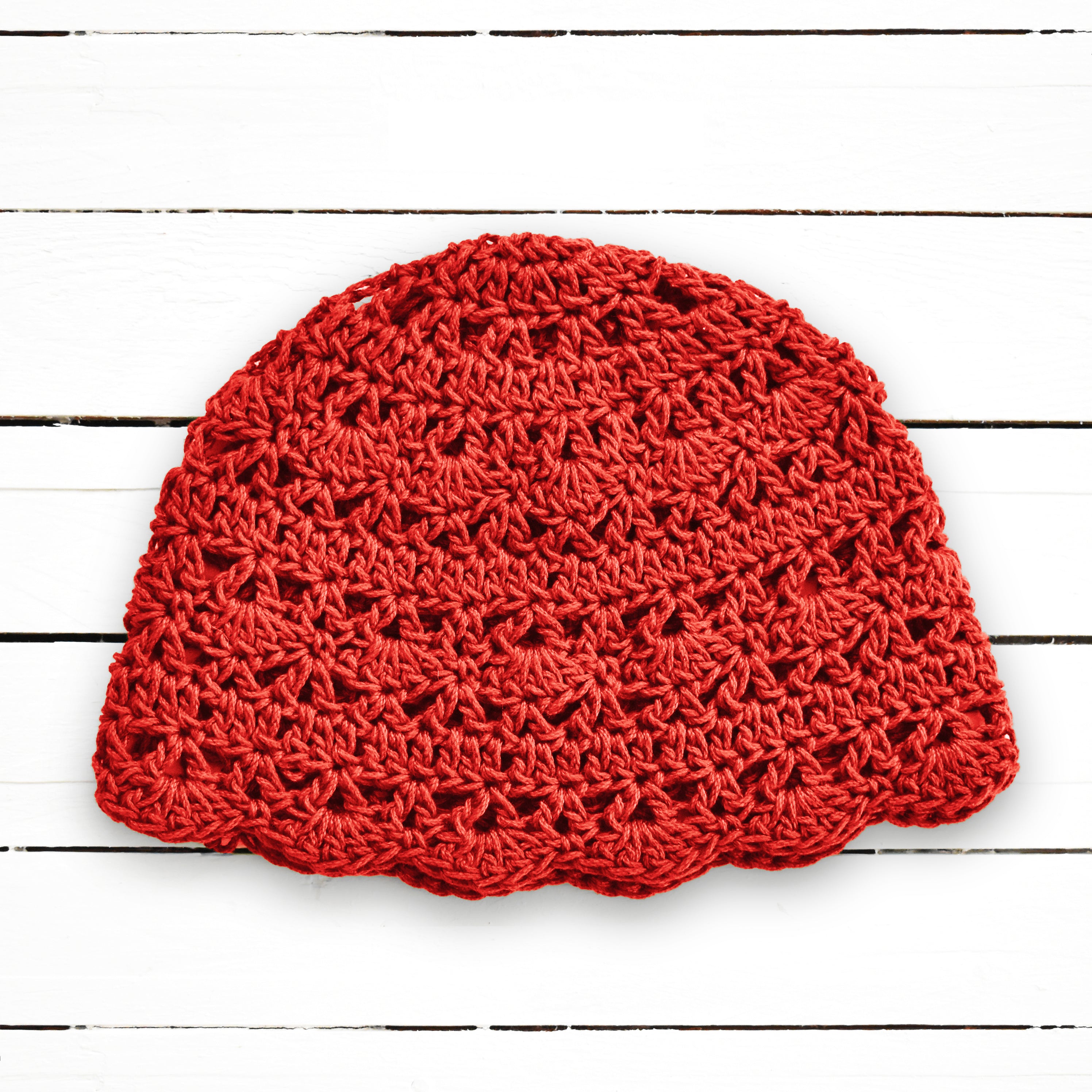 Red crocheted boho beanie on a white wooden surface.