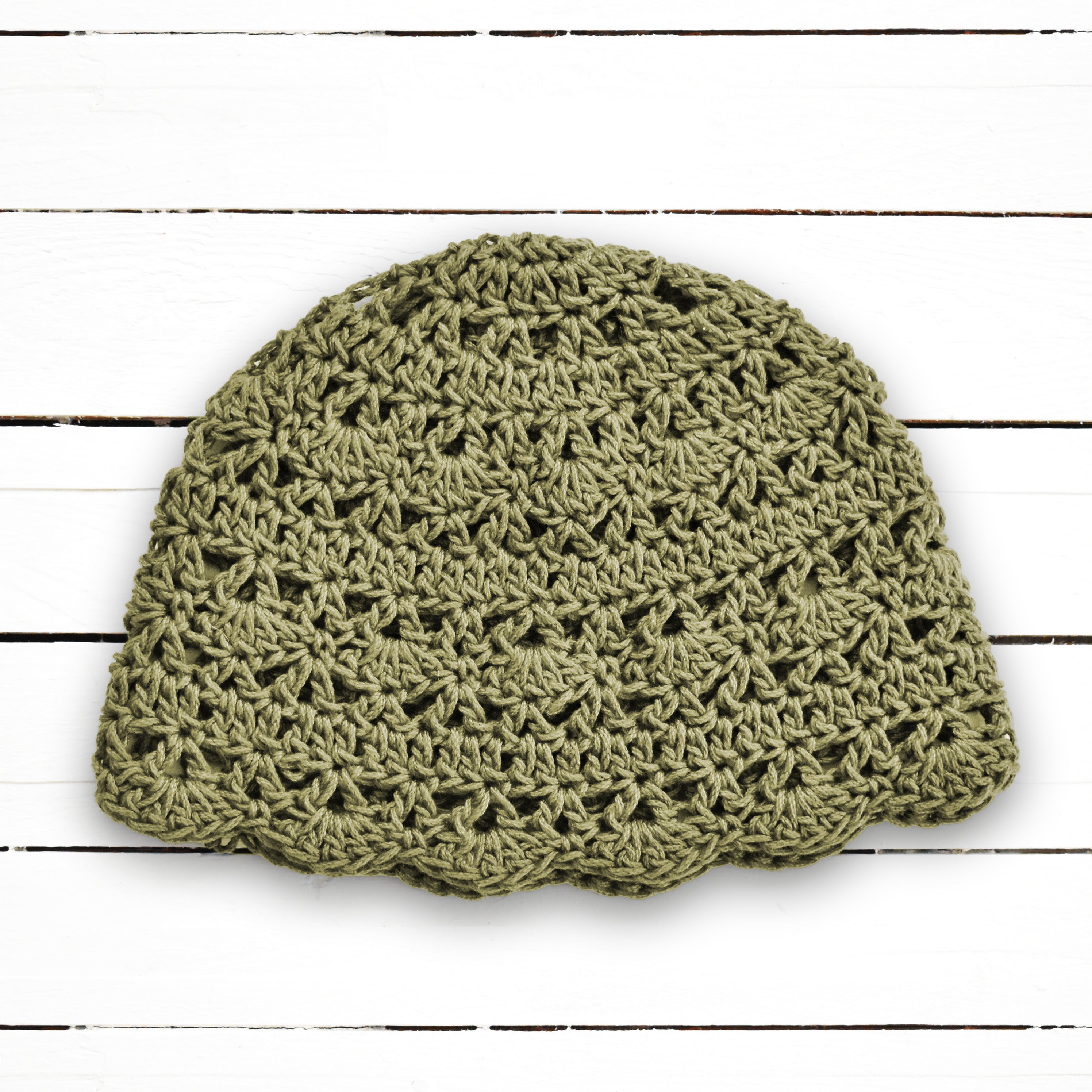Crocheted sage green beanie on a white wooden background.