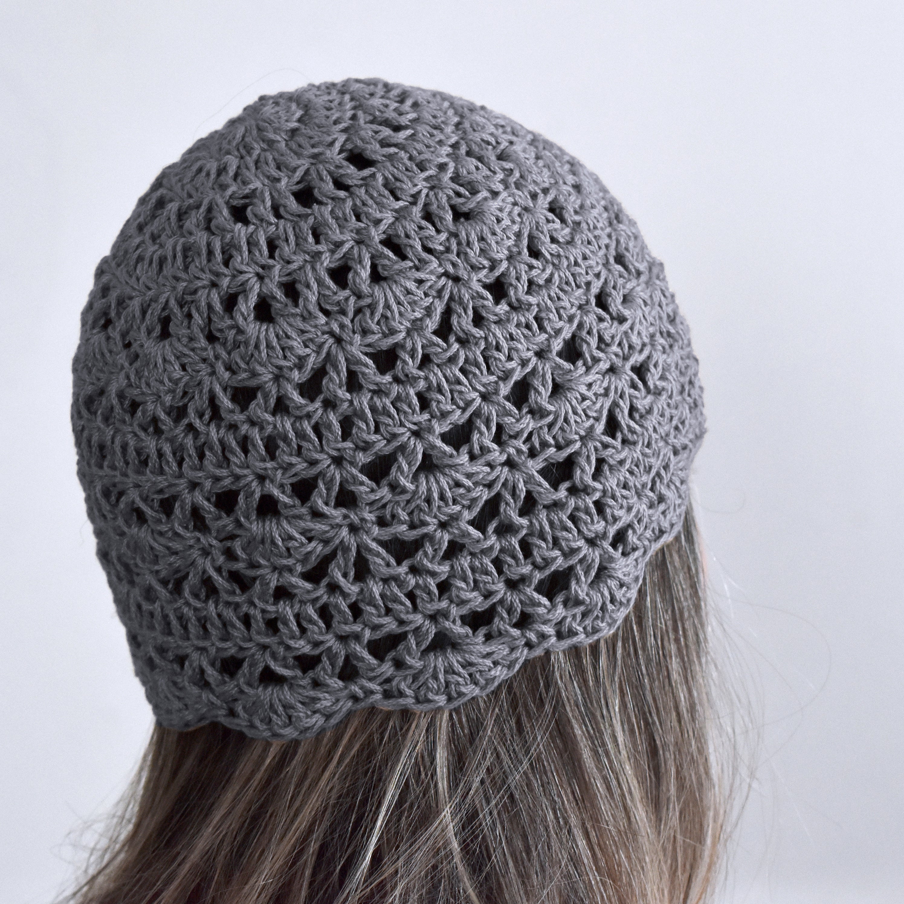 Gray knitted beanie on a person with long hair against a neutral background.