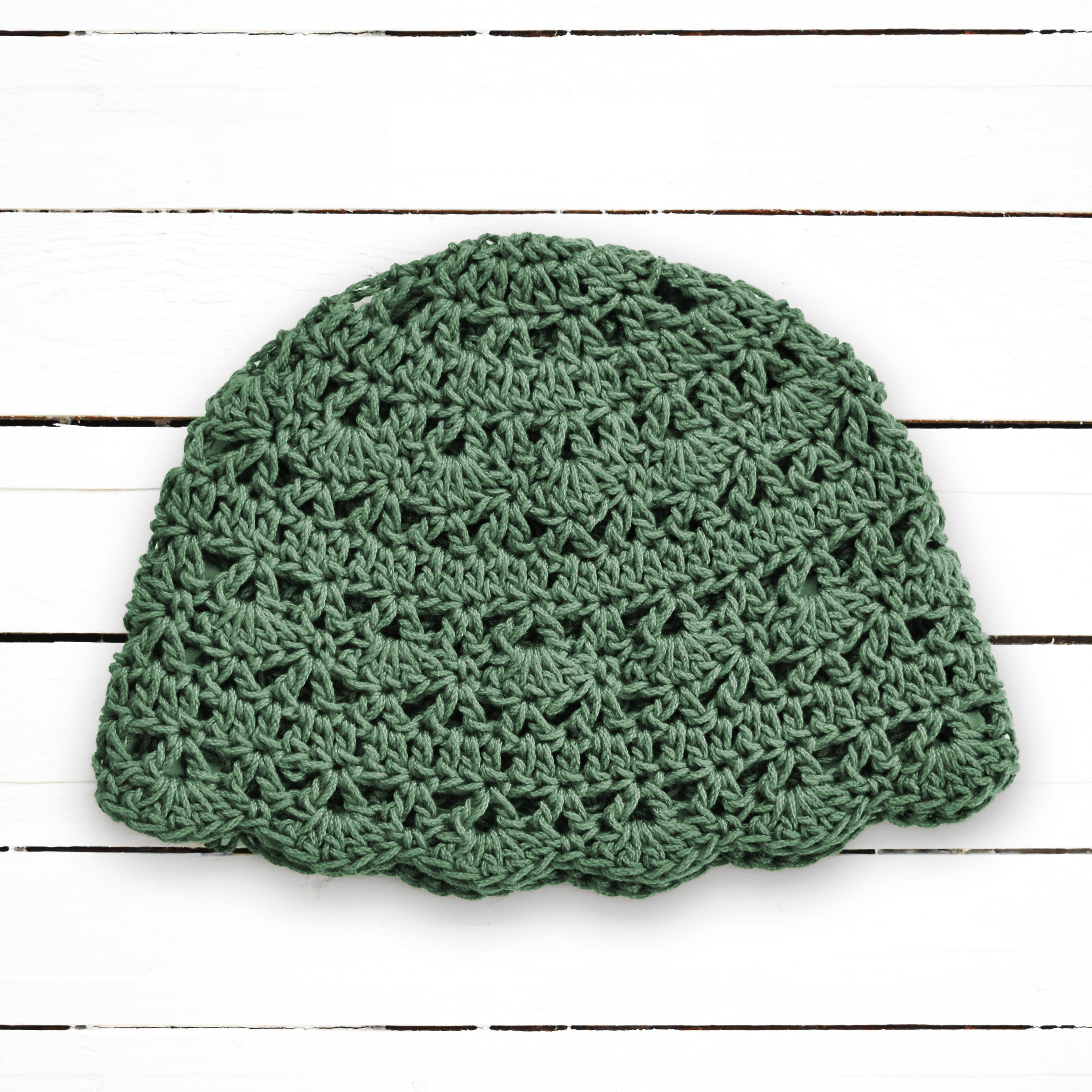 Green crocheted beanie on a white wooden surface.