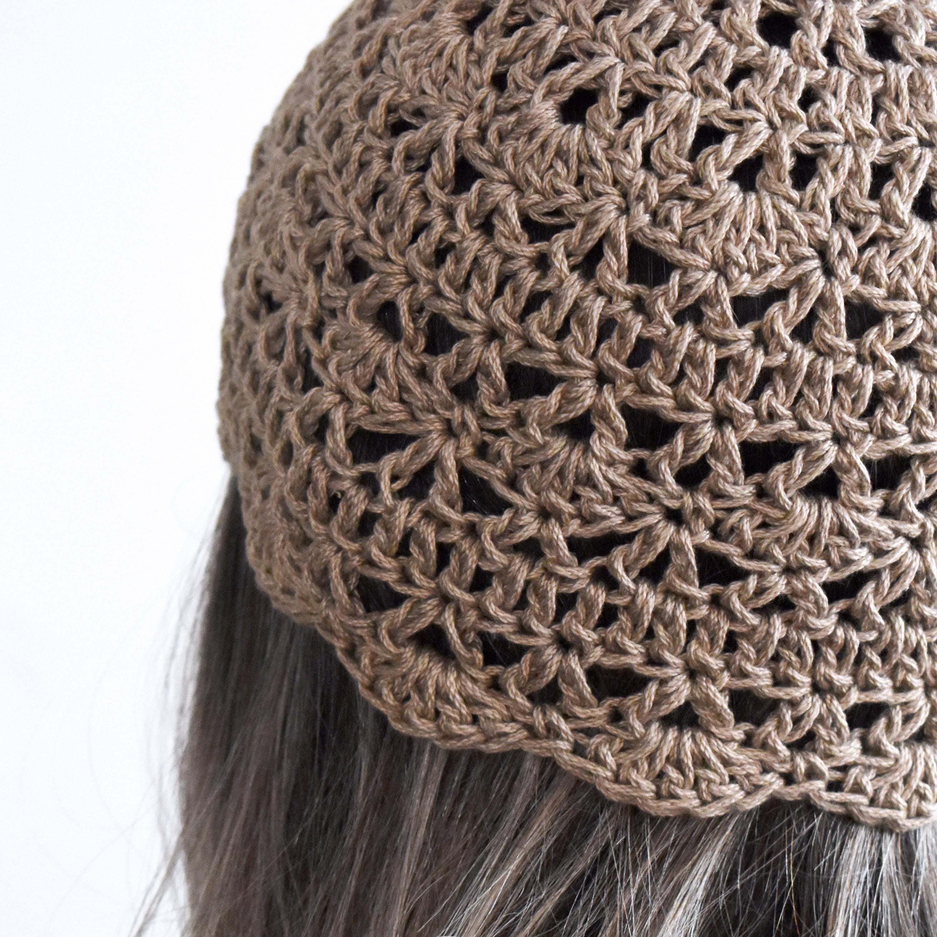 Close-up of a light brown knitted hat on a person with gray hair.