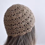 Taupe crochet beanie worn by a person with gray hair on a white background.