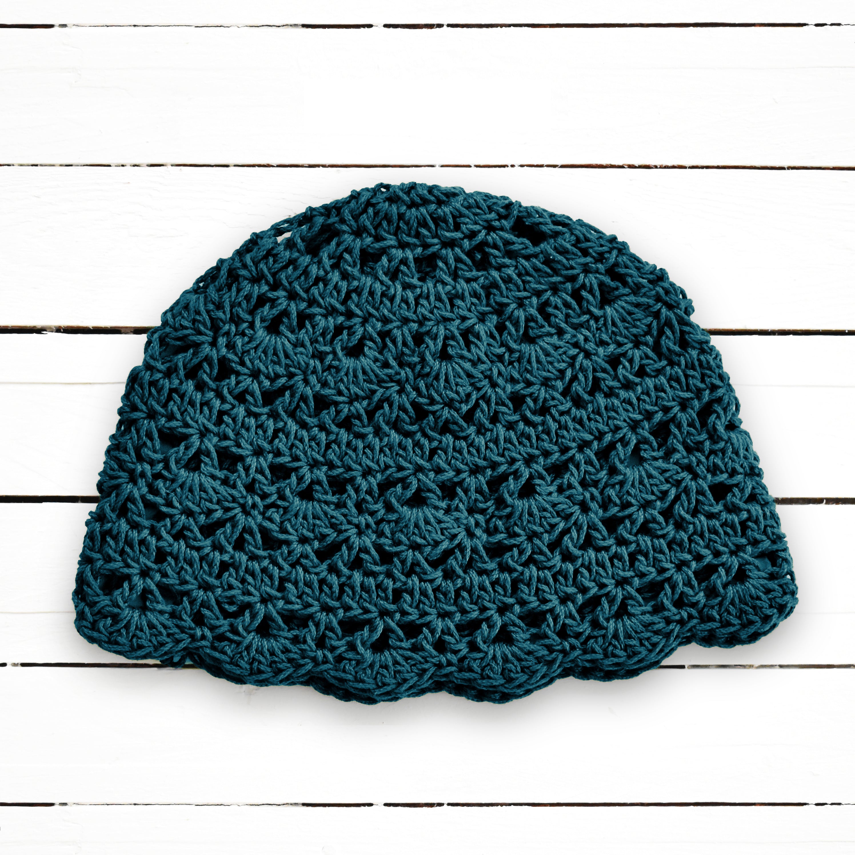 Teal crochet beanie on a wooden surface.
